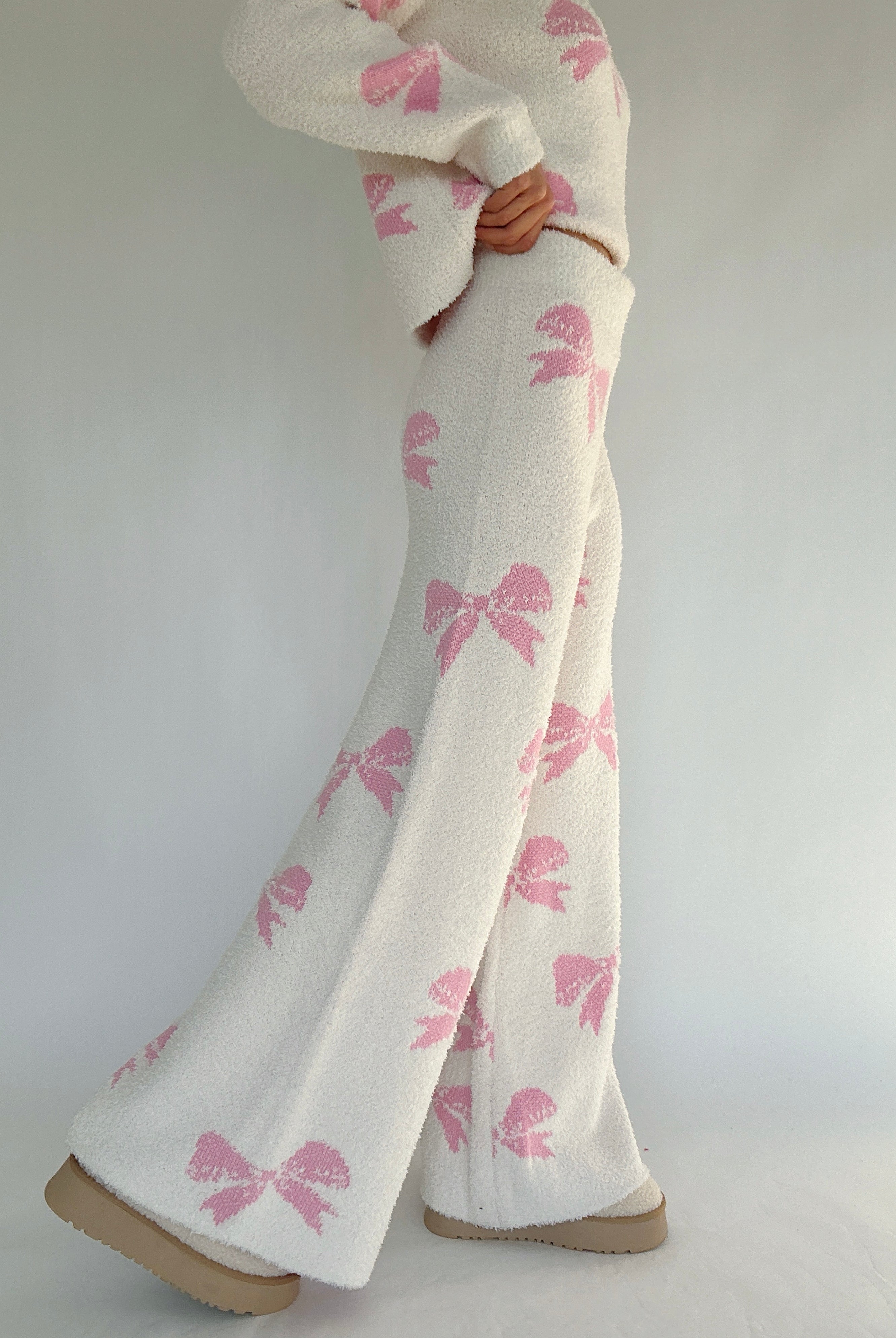 White pants with pink bow patterns worn by a person on a plain background showing side of pants