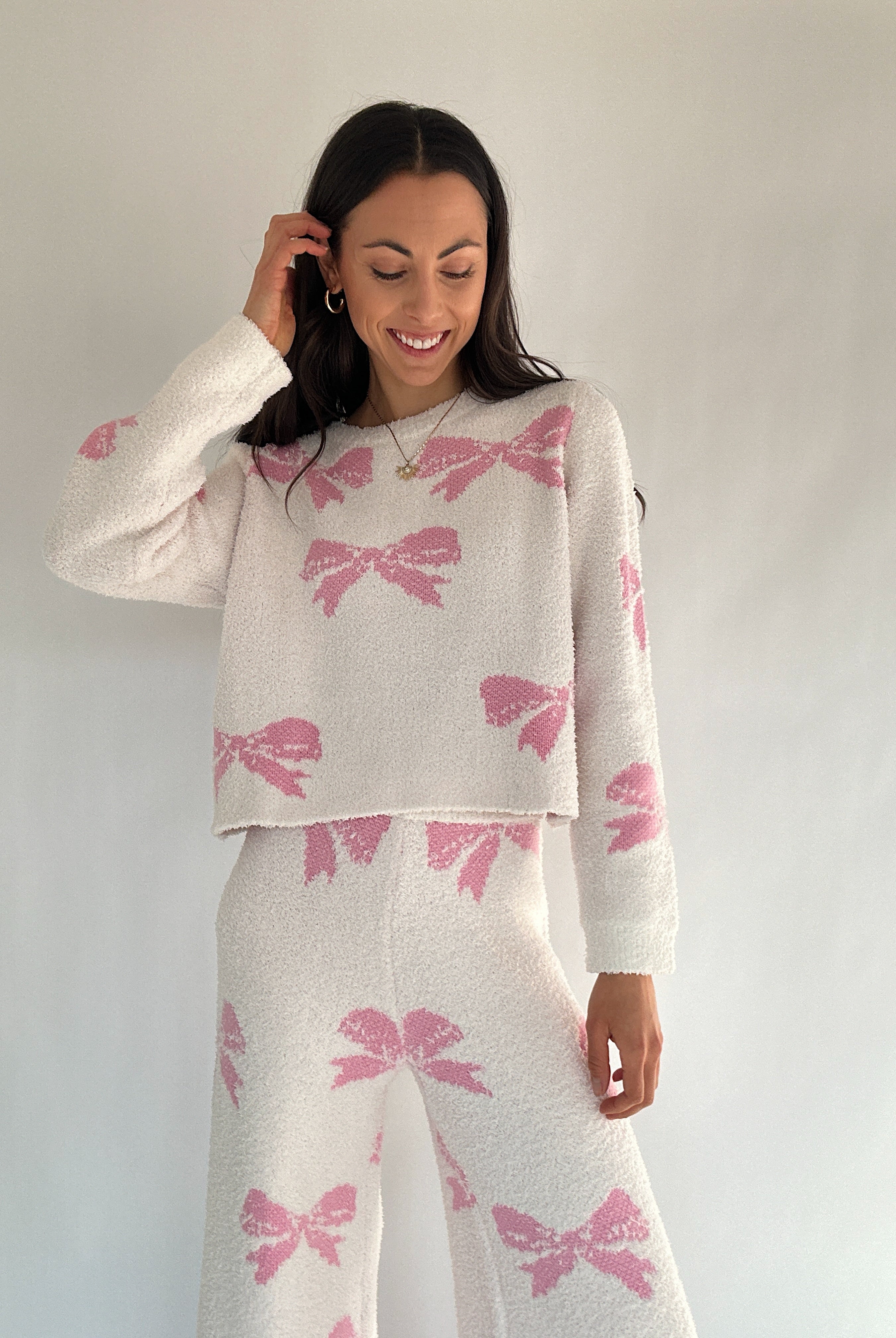 Woman wearing a white sweater and skirt with pink bow patterns against a plain background