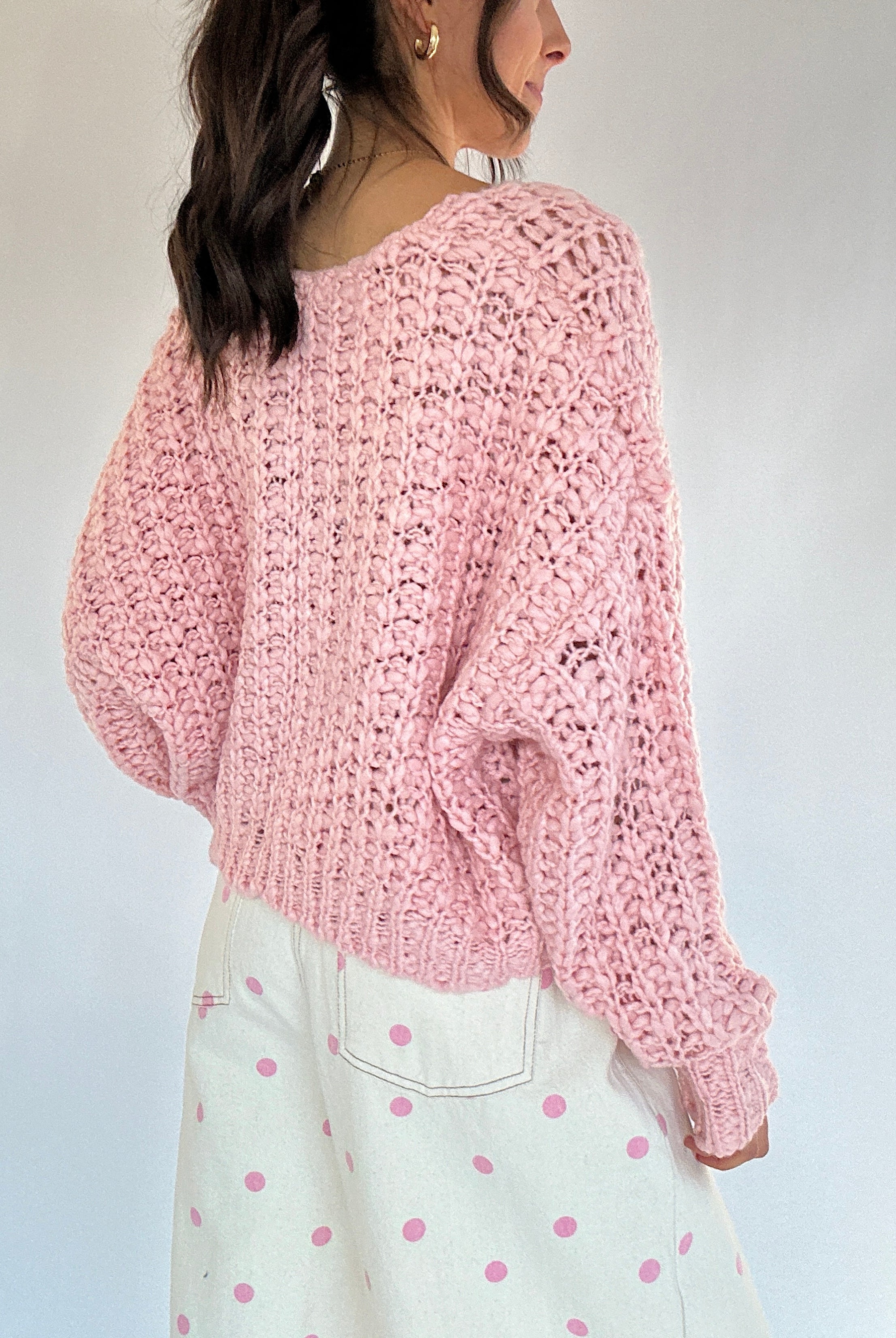 Person wearing a pink knitted sweater and white pants with pink polka dots against a plain background back view