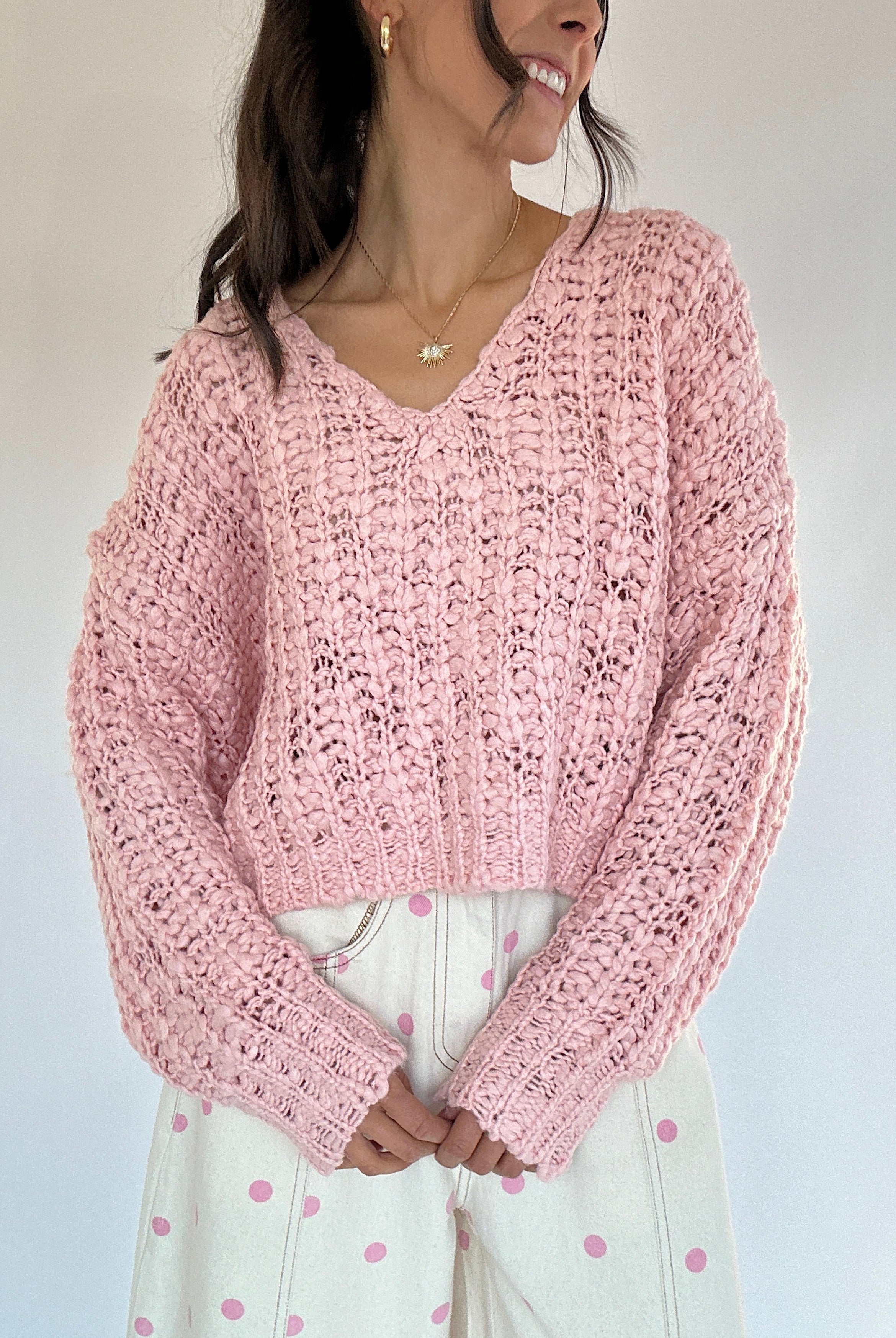 Person wearing a pink knitted sweater against a plain background