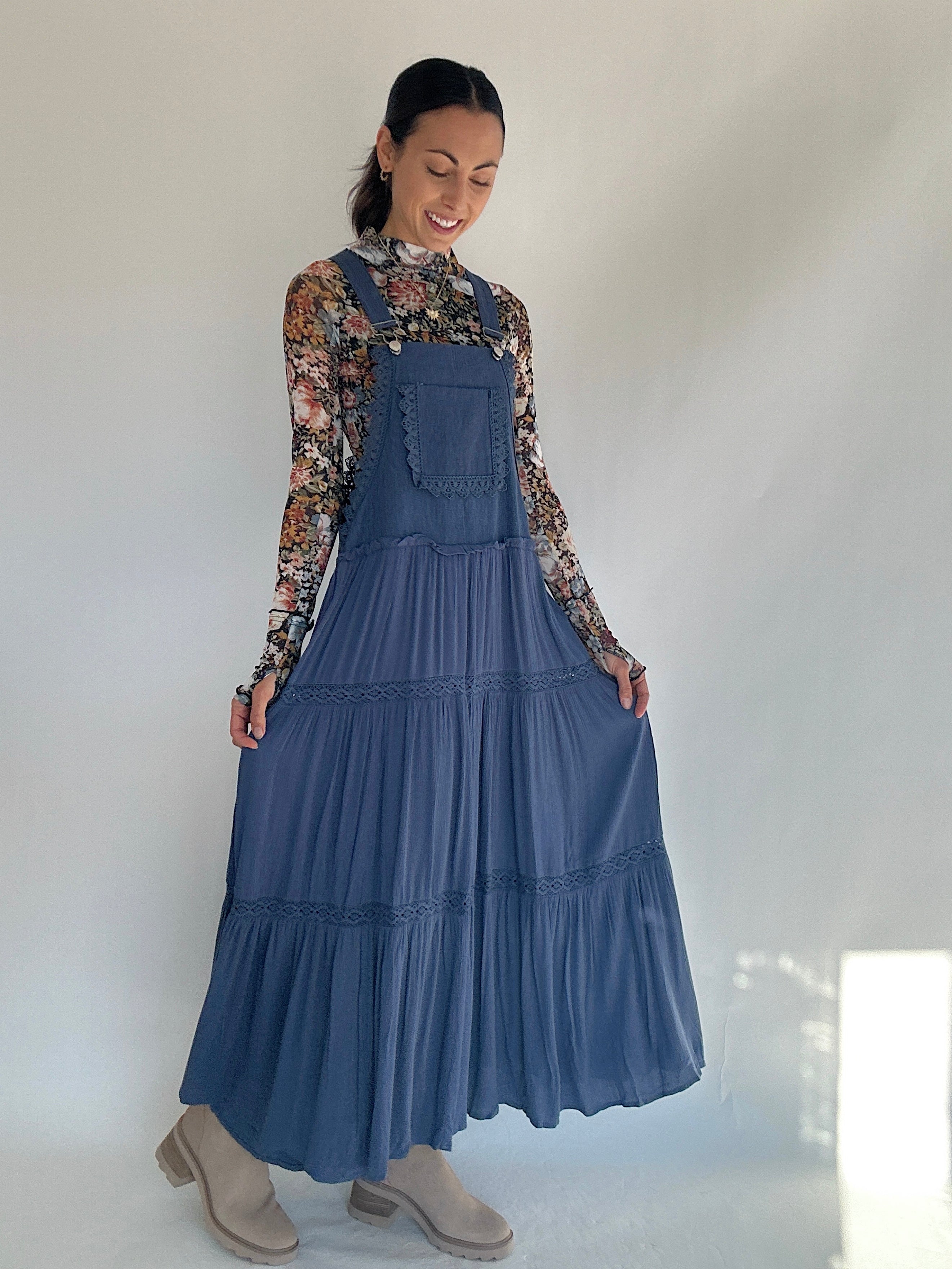 Woman wearing a blue tiered overall dress with a floral blouse against a white background