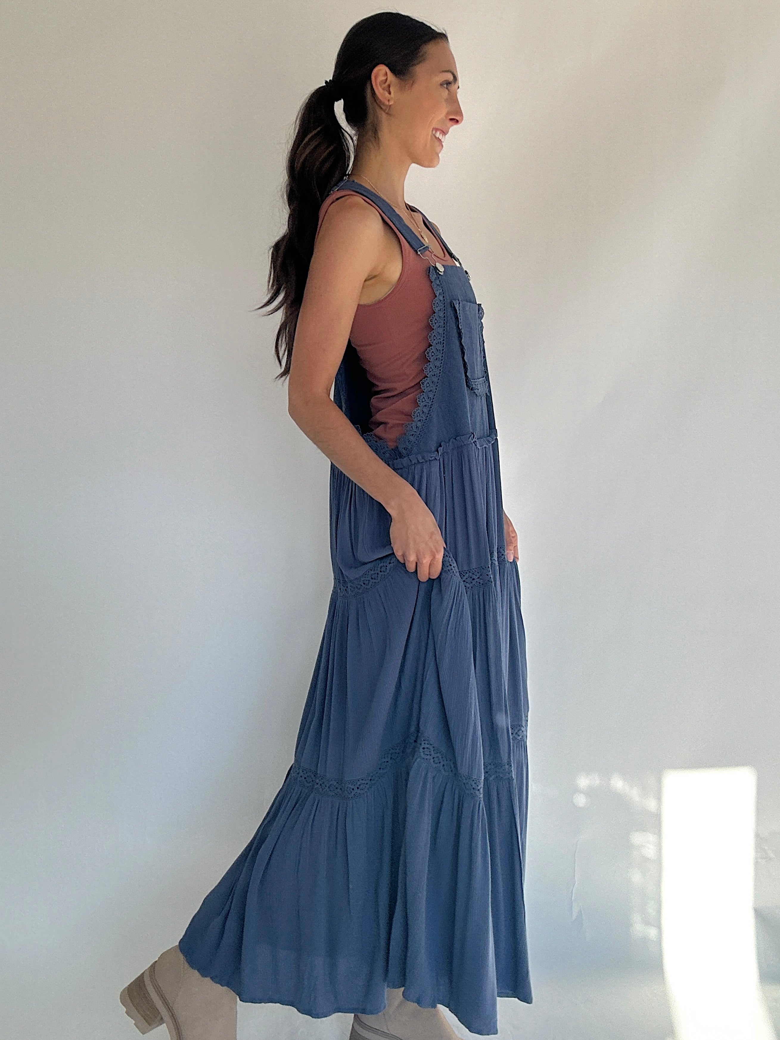 Woman wearing a long blue dress with a white background to show off side view with a tank top underneath