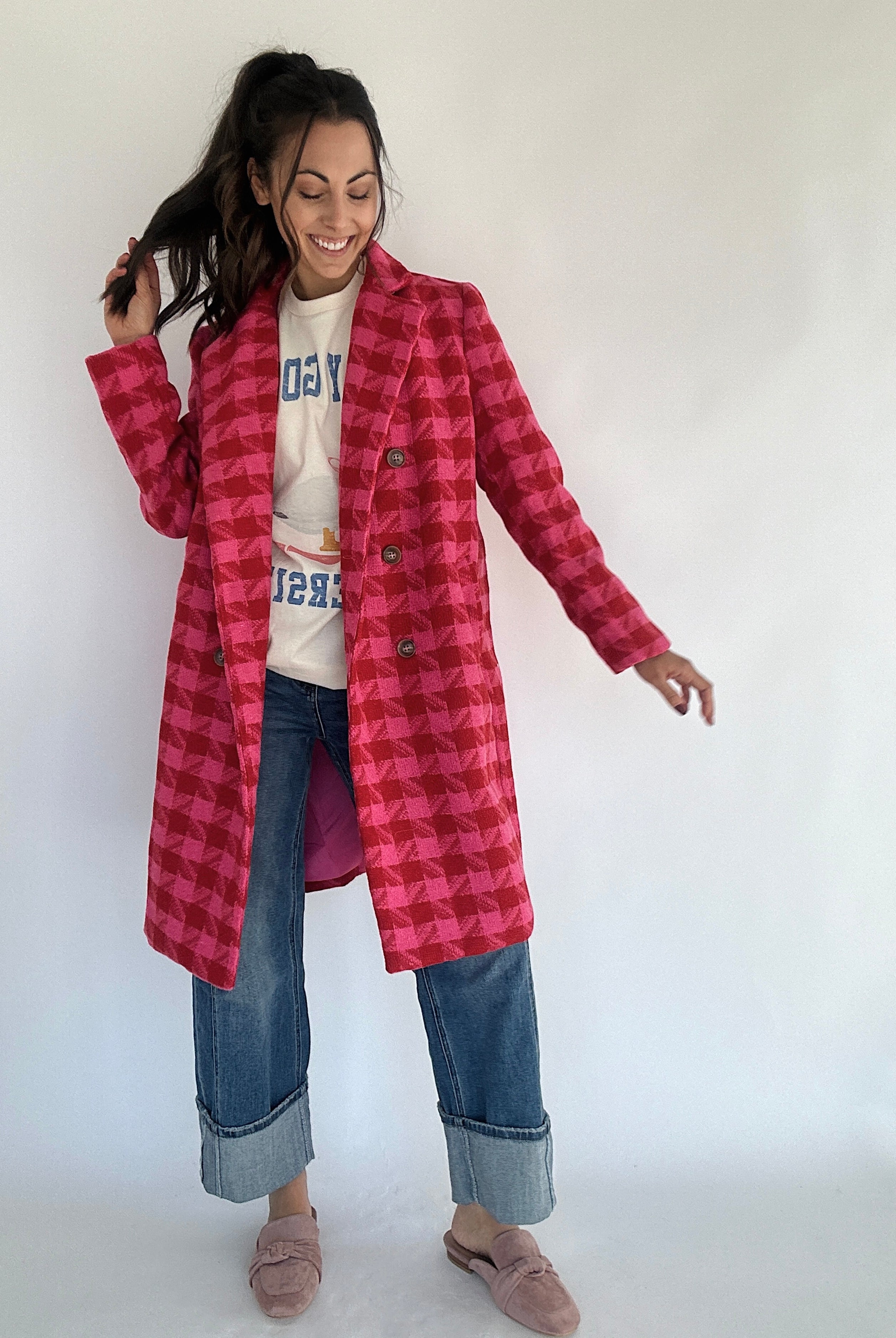 Woman wearing a hot pink and red houndstooth tweed coat over a graohic tee and jeans