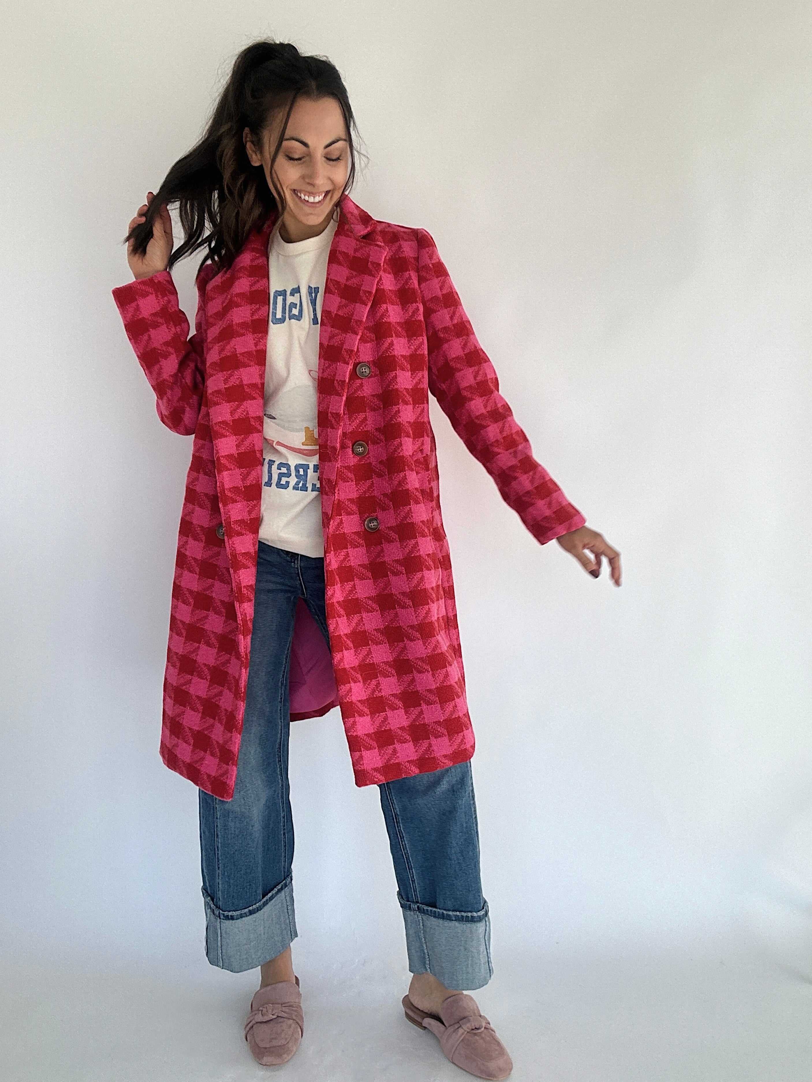 Woman wearing a hot pink and red houndstooth tweed coat over a graohic tee and jeans