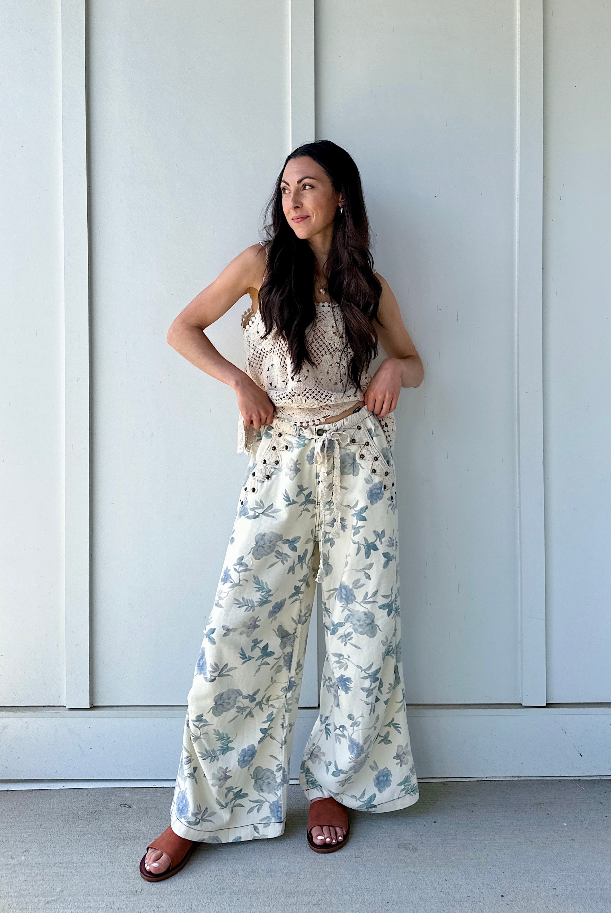 Woman wearing cream and blue floral pants standing against a white wall.