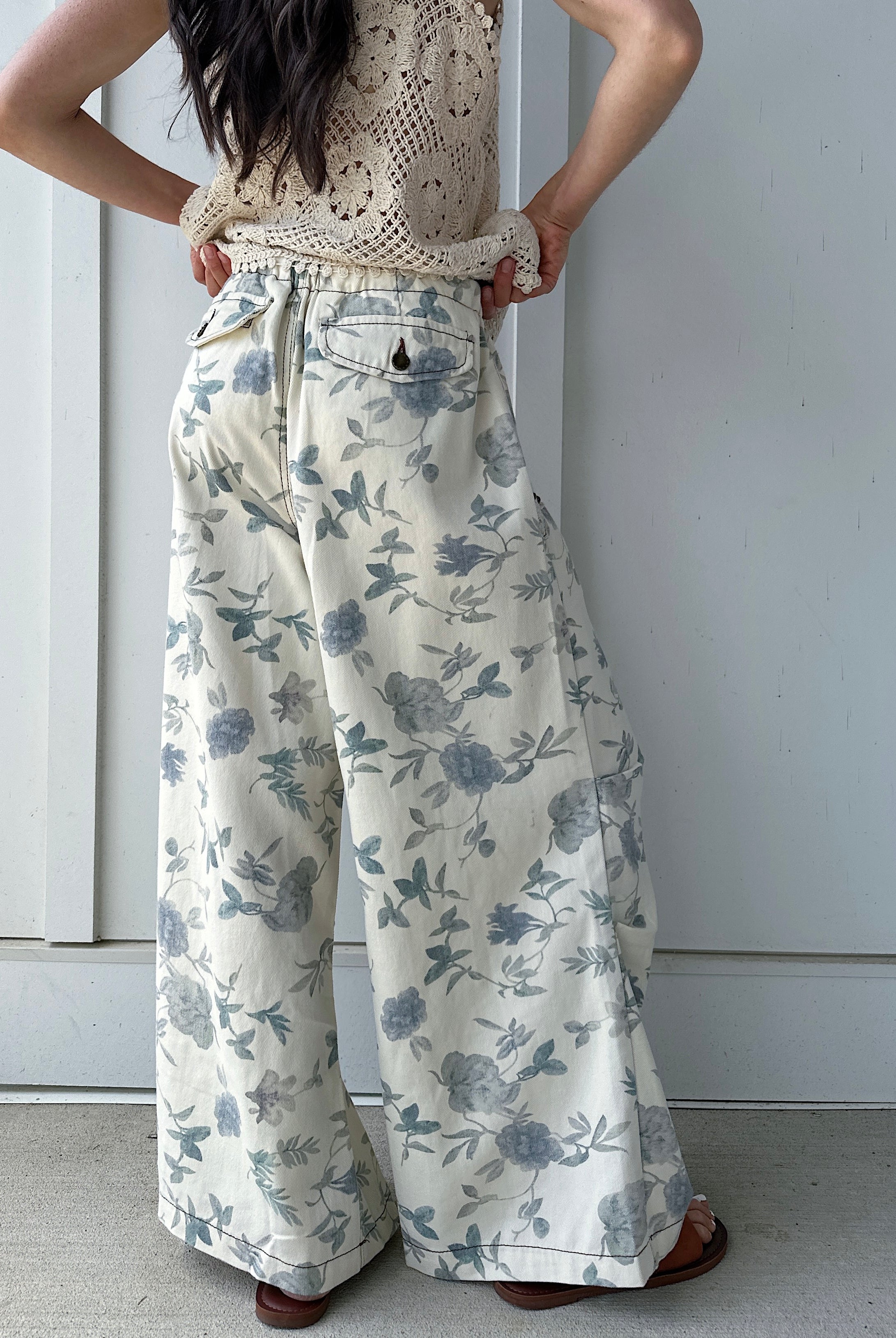 Person wearing a beige crochet top and floral wide-leg pants showing the back pocket details against a white background