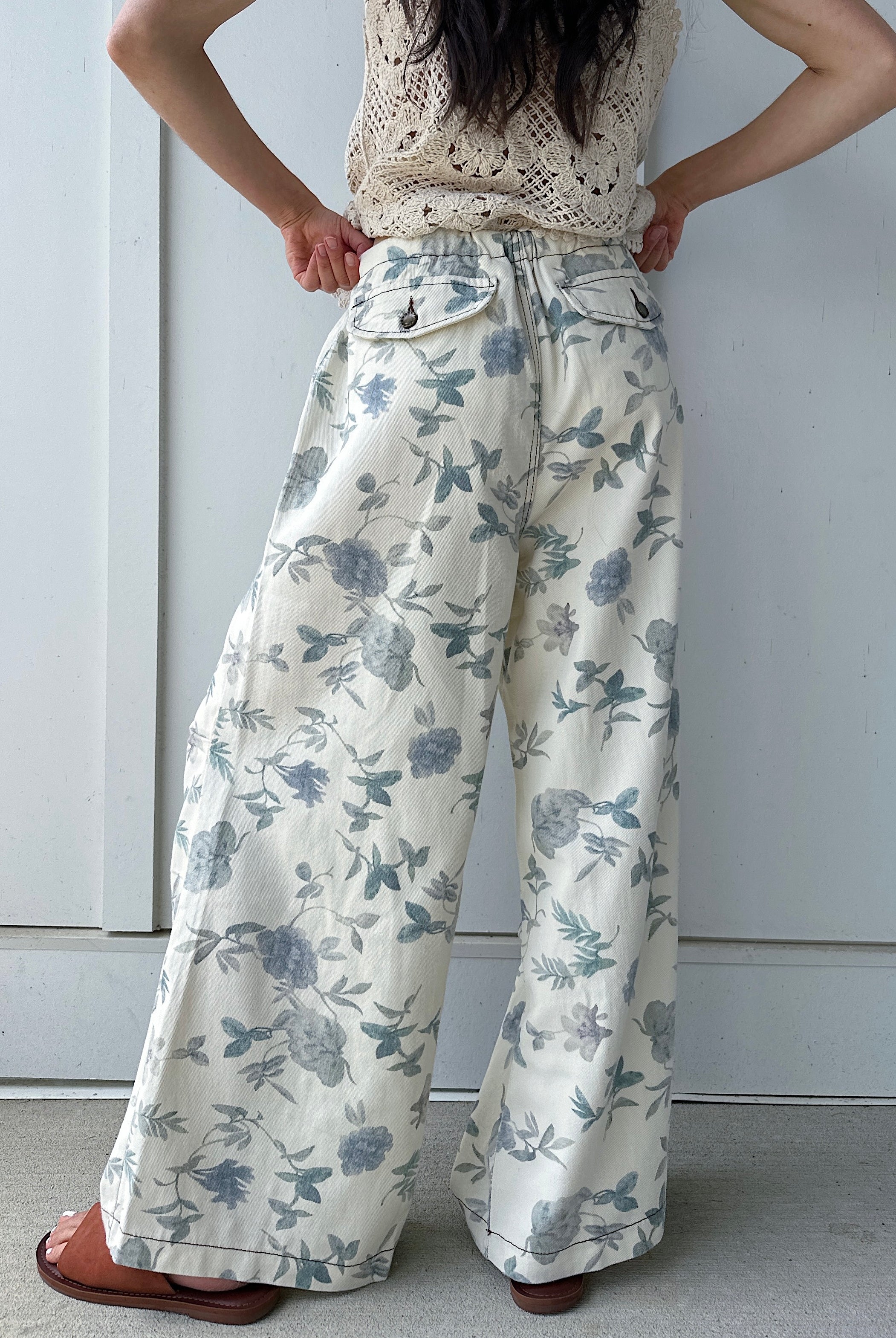 Person wearing floral wide-leg pants from back against a plain background