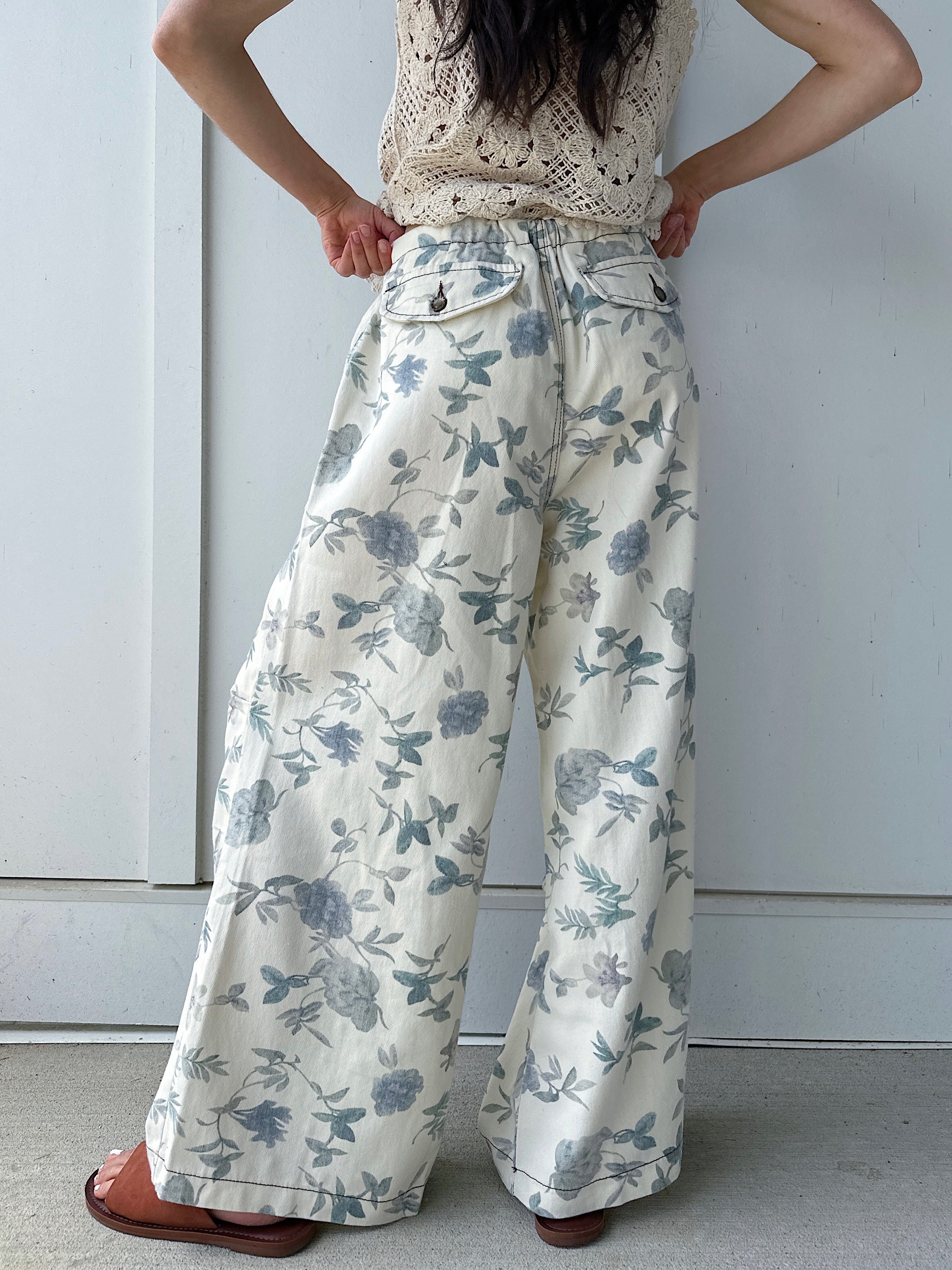 Person wearing floral wide-leg pants from back against a plain background