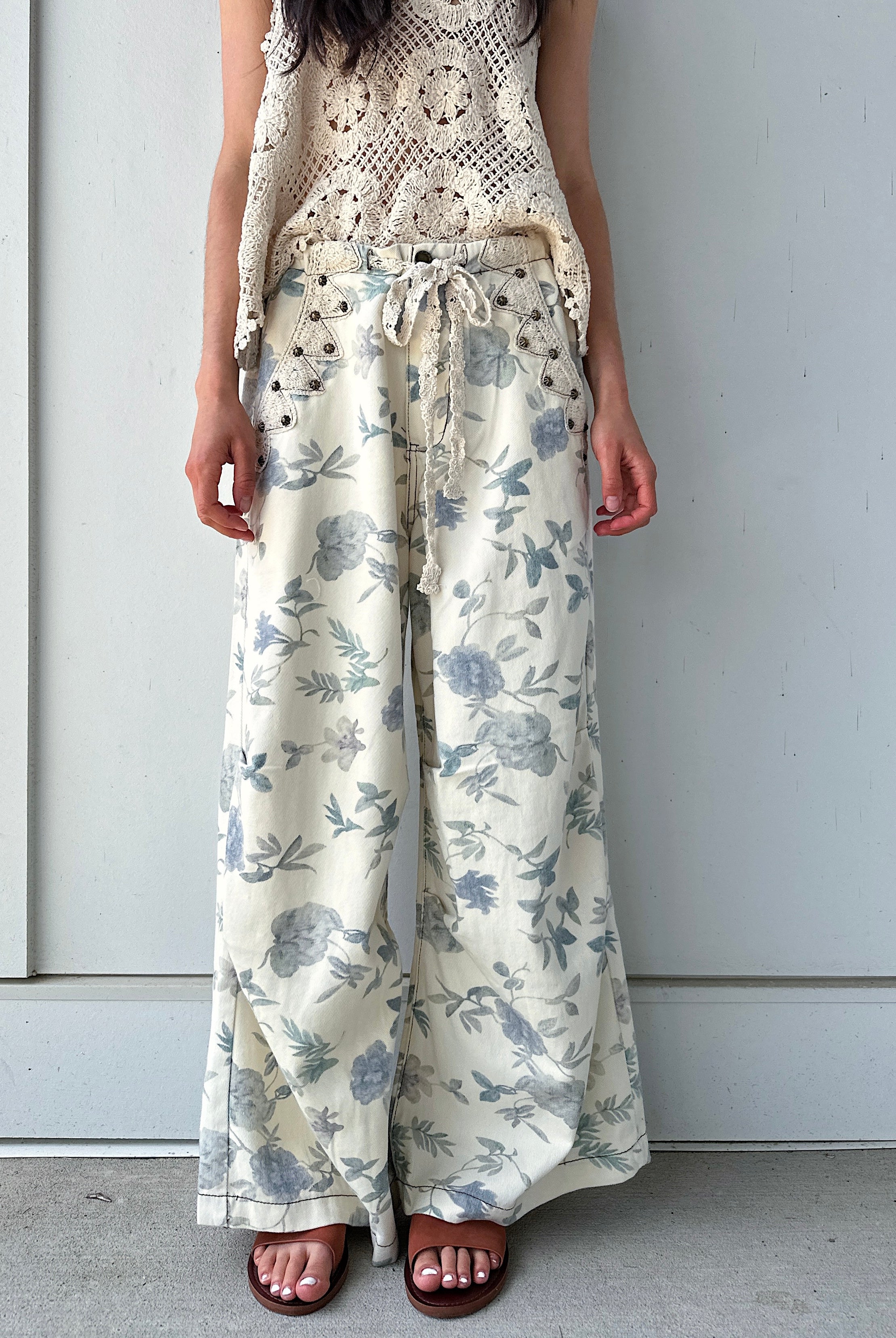 Person wearing cream and white floral wide-leg pants against a plain background