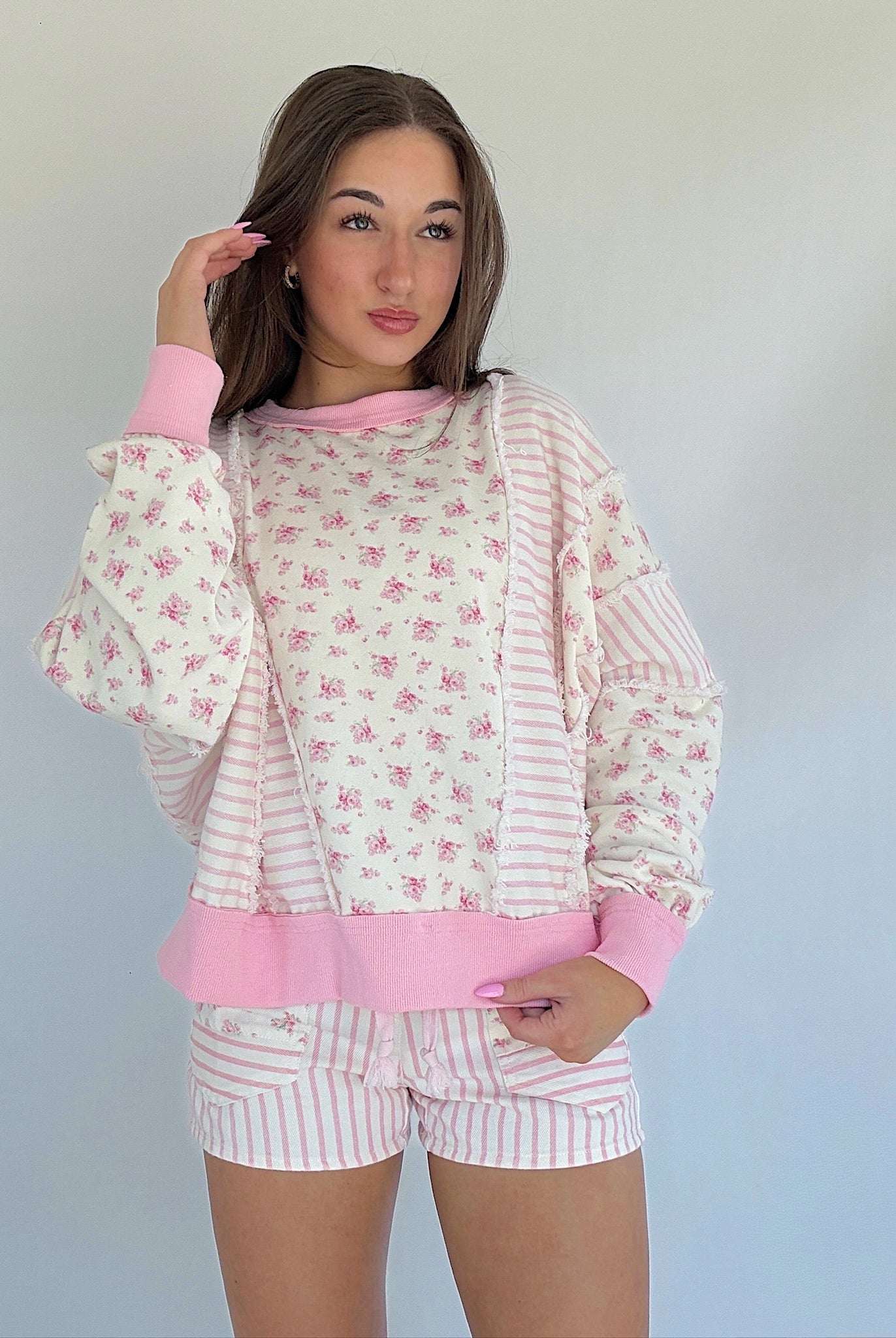 Woman wearing a pink and white floral matching pullover and shorts against a plain background