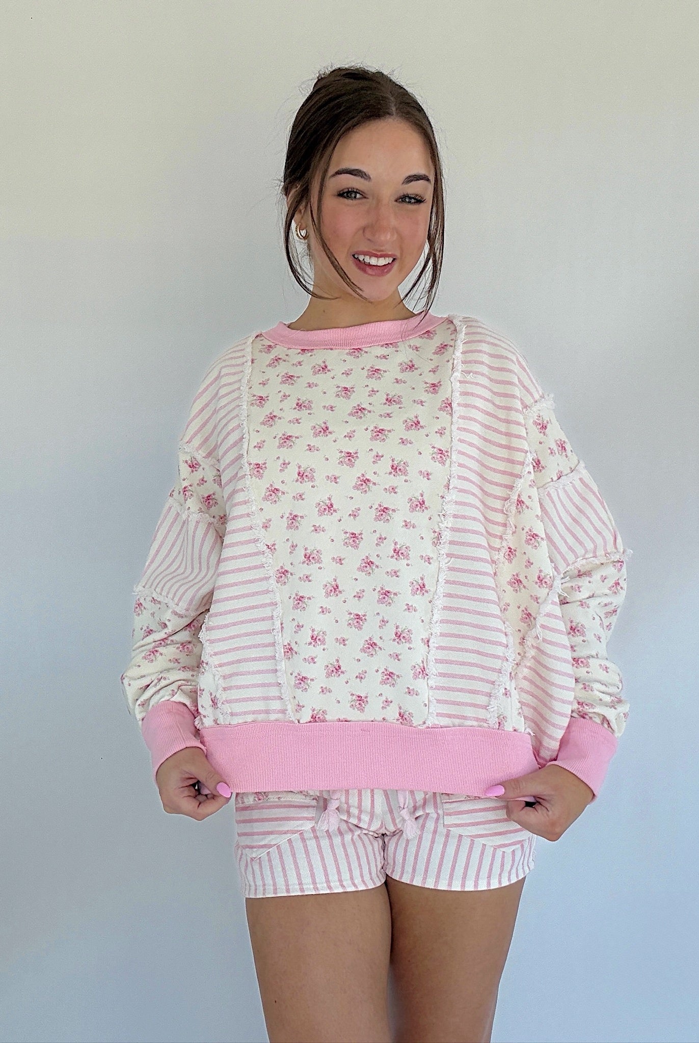 Woman wearing a pink and white pullover top with a floral pattern against a plain background