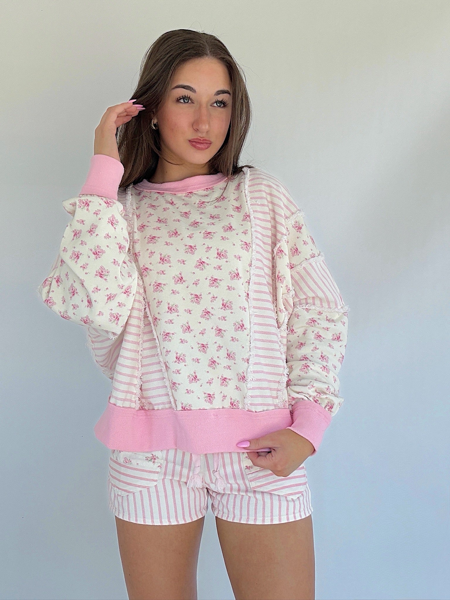 Woman wearing a pink and white floral pullover with matching shorts against a plain background