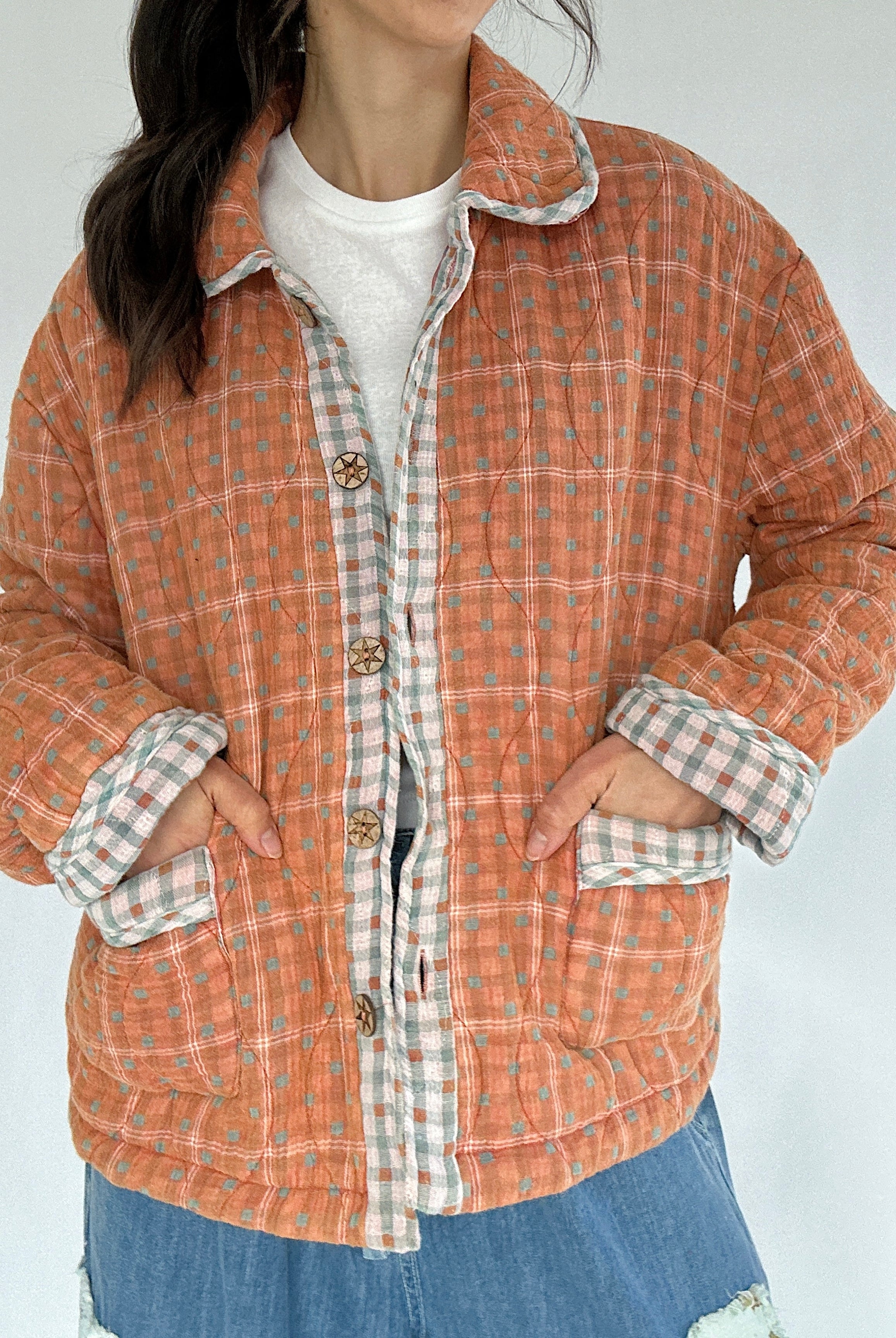 Person wearing a rust orange plaid jacket that has contrast trim and wood buttons with a white background