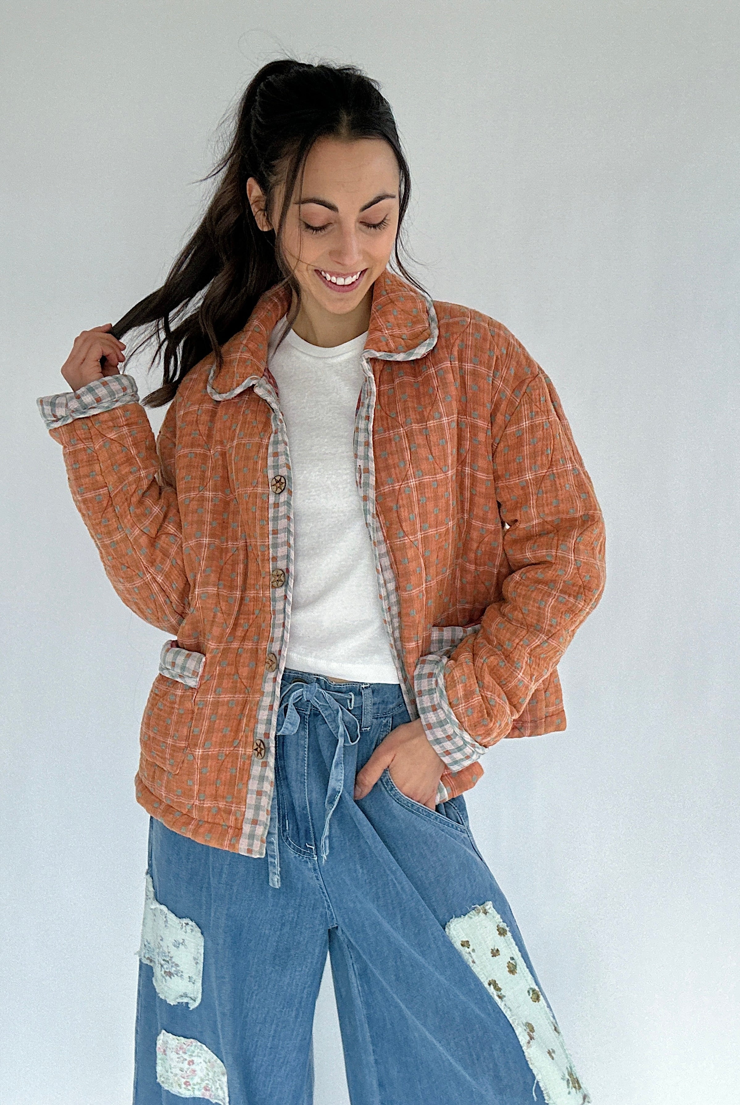 Woman wearing a rust orange plaid jacket and blue jeans against a white background