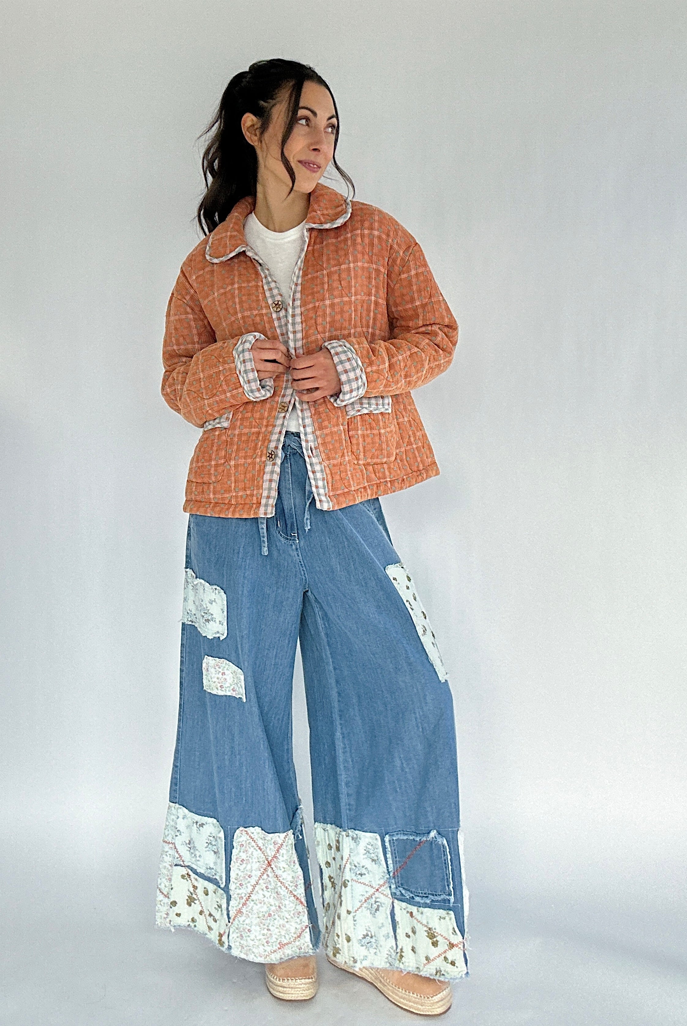 Person wearing a checkered jacket and blue denim pants with floral patterns on a plain background