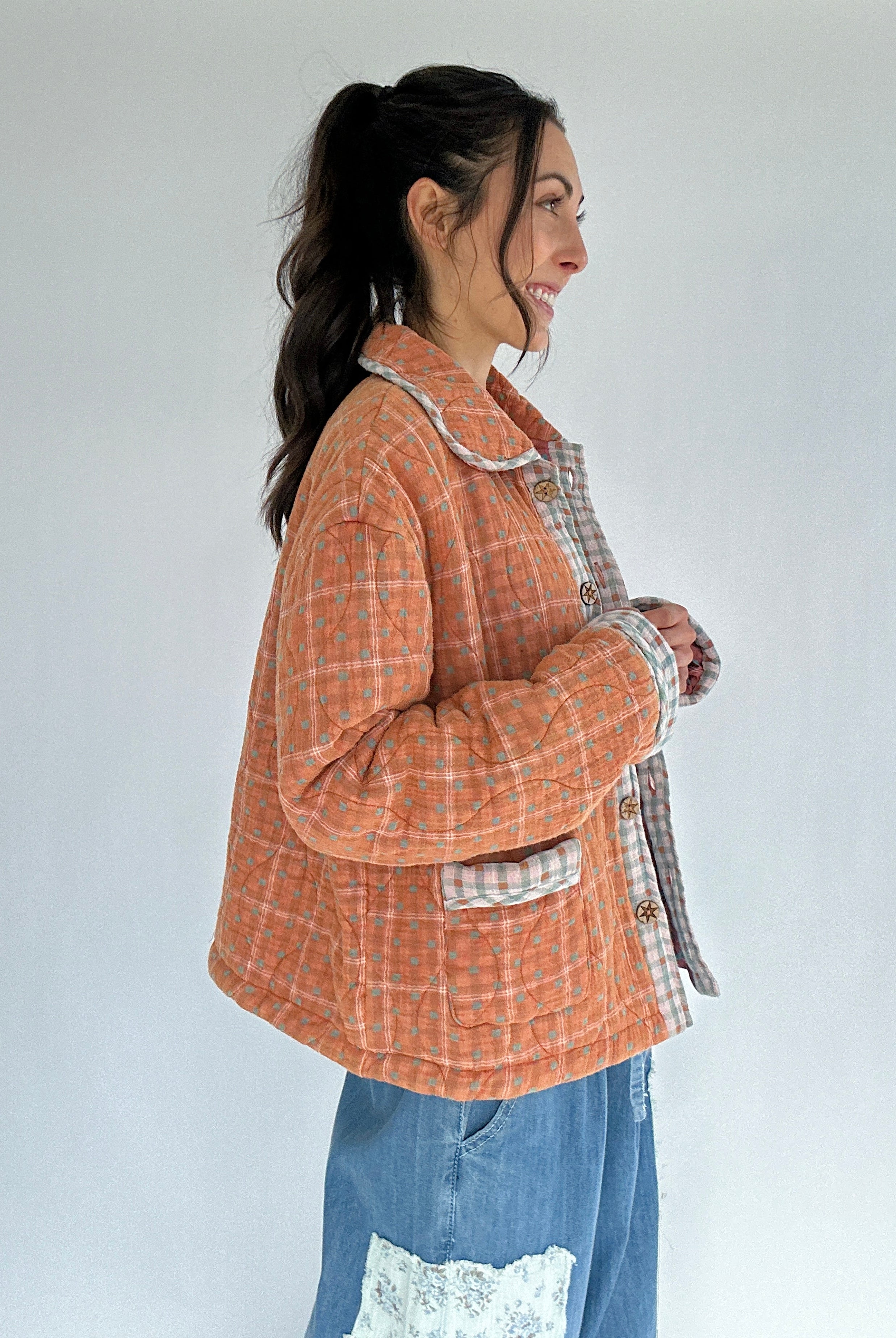 Woman wearing a checkered jacket over a plaid shirt with a white background from side