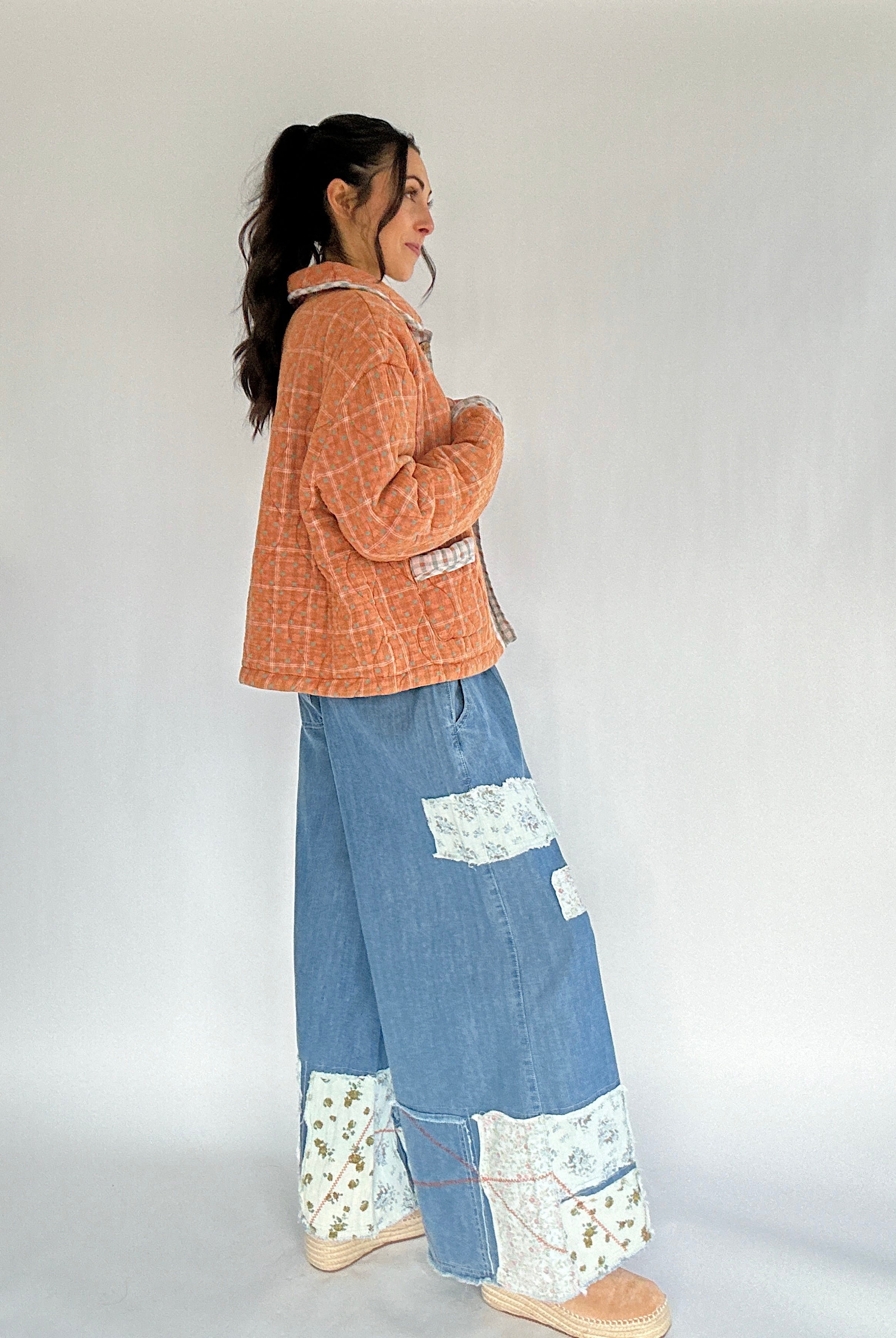 Person wearing a rust orange plaid jacket and blue patchwork pants on a white background