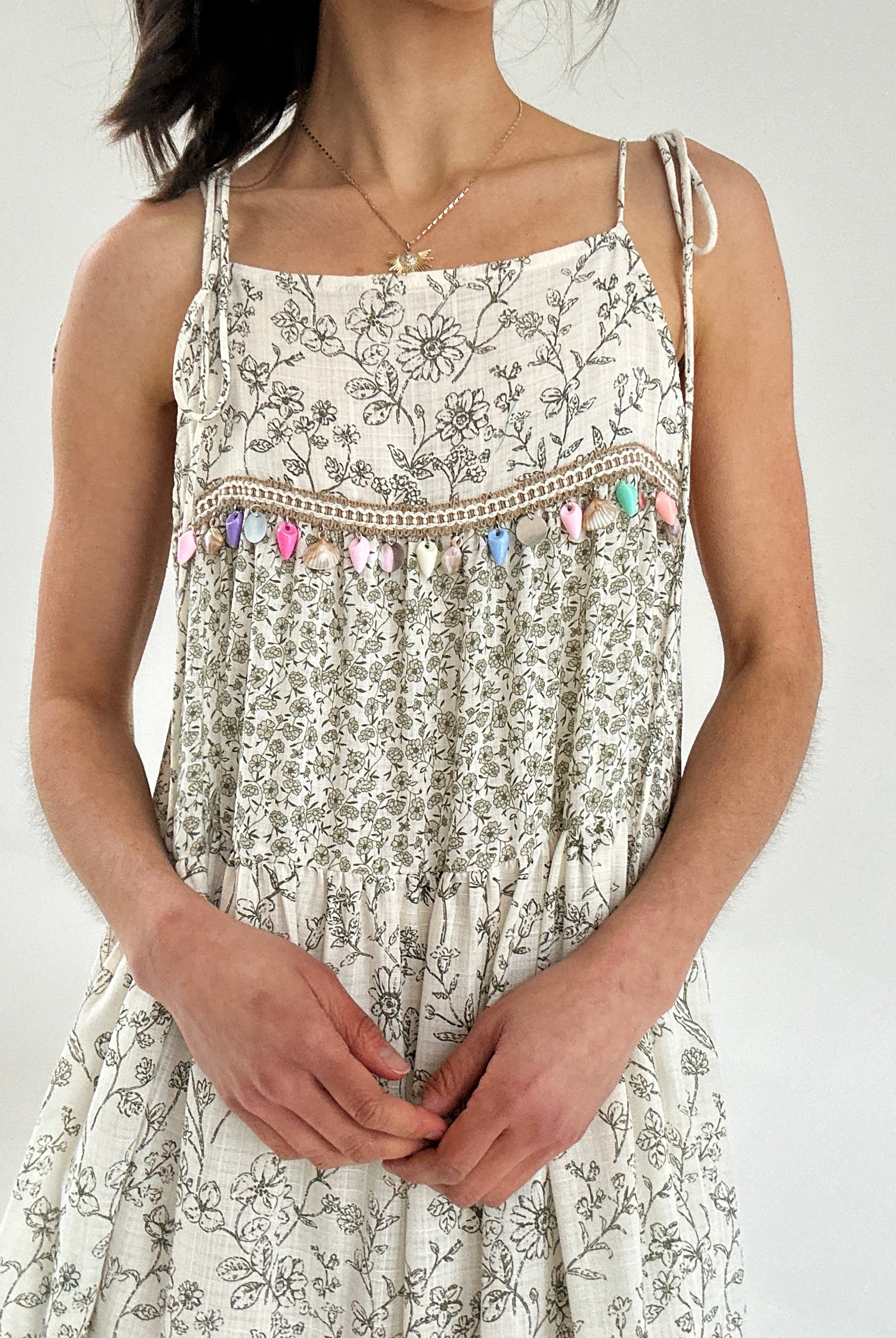 Woman wearing a floral dress with decorative straps against a white background