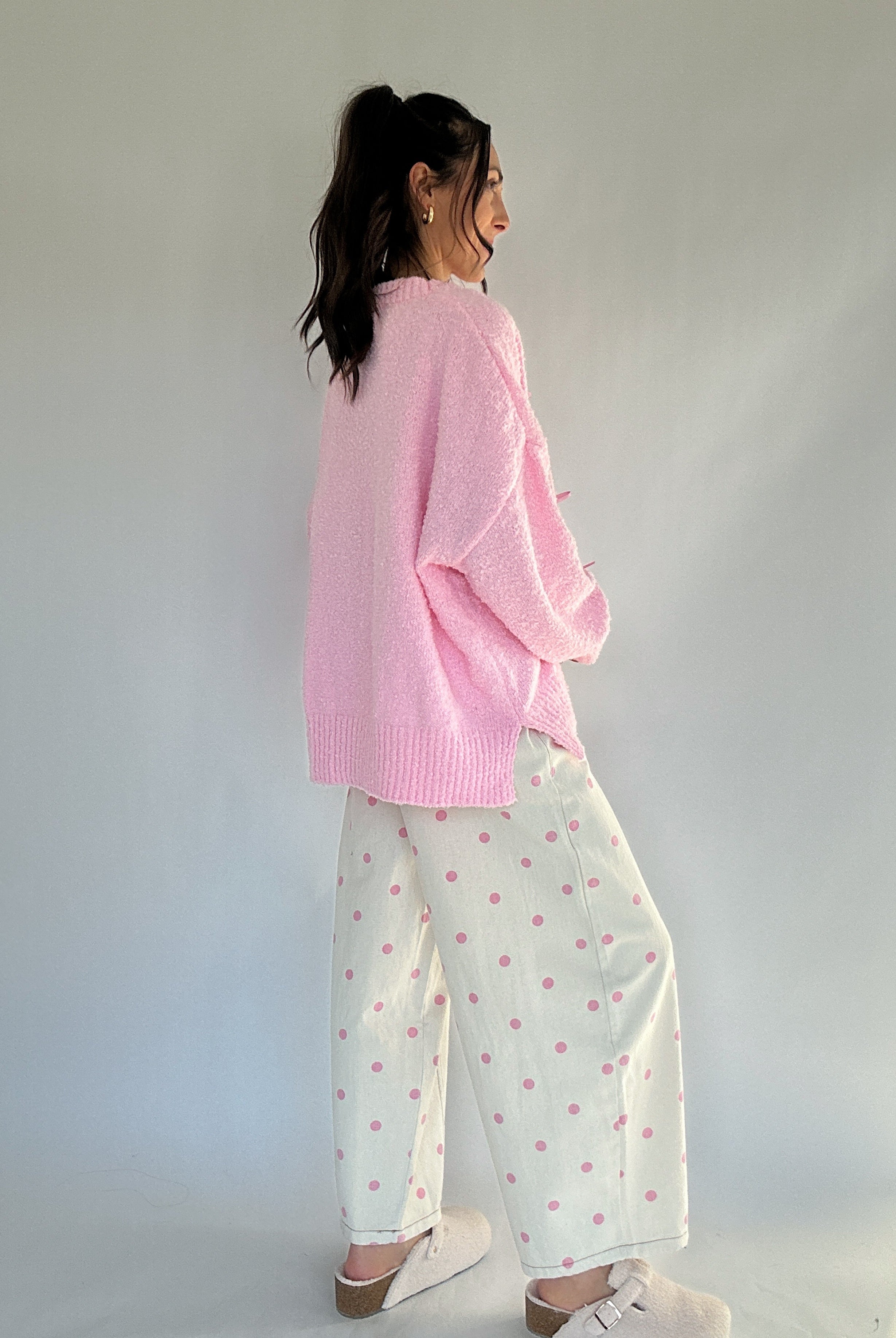 Woman wearing a pink sweater and polka dot pants with a subtle pattern against a plain background