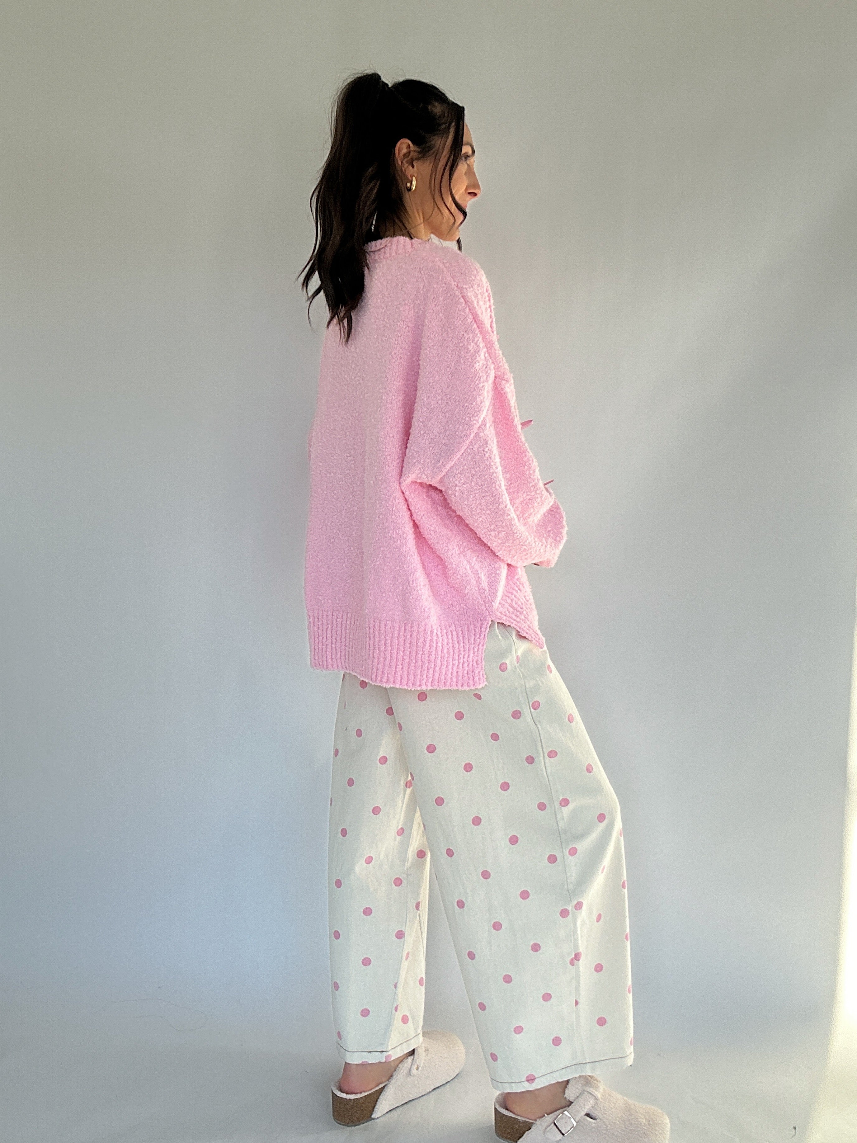 Woman wearing a pink sweater and polka dot pants with a subtle pattern against a plain background