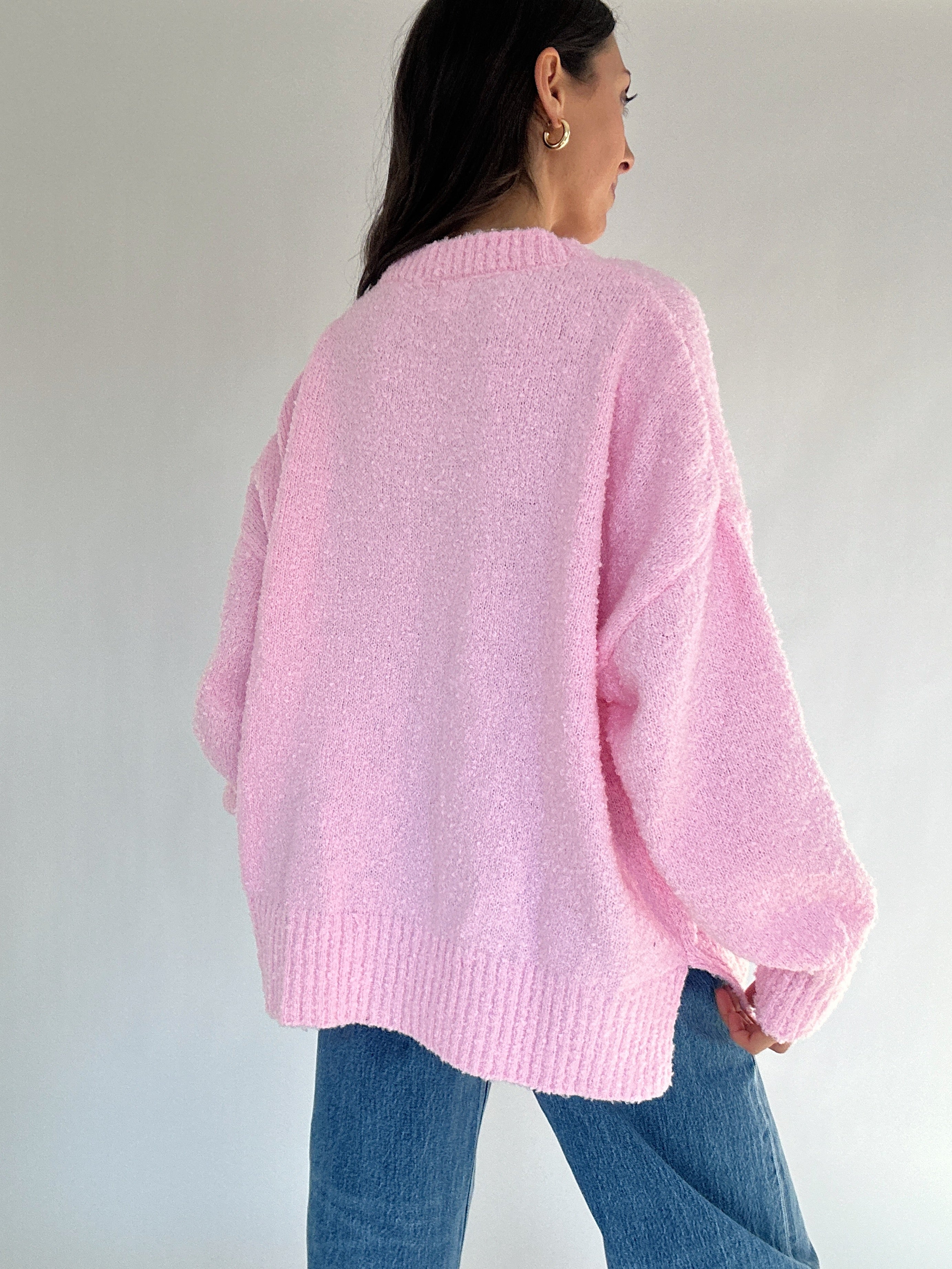 Person wearing a pink sweater and blue jeans against a plain background