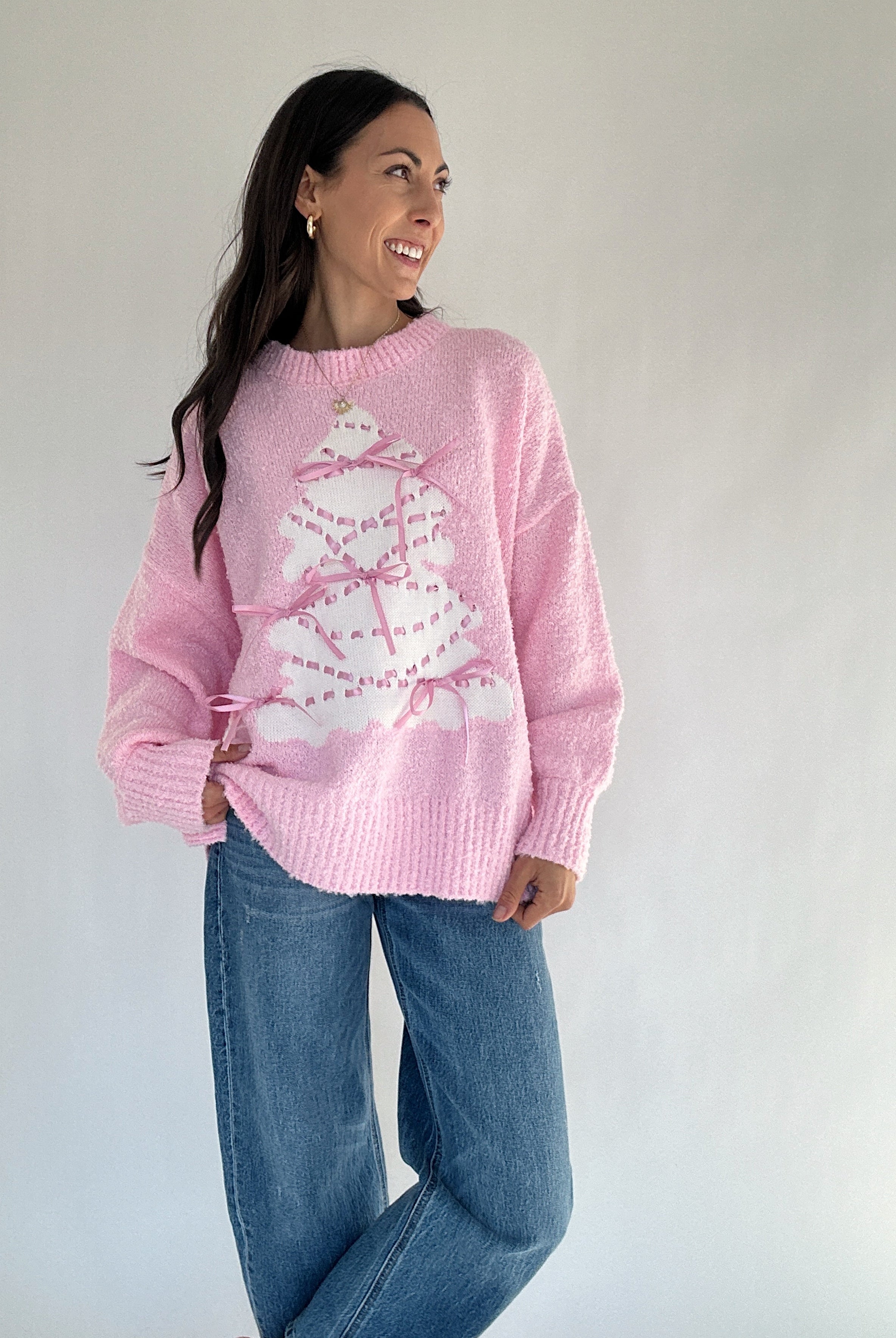 Woman wearing a pink sweater with a white tree design against a plain background