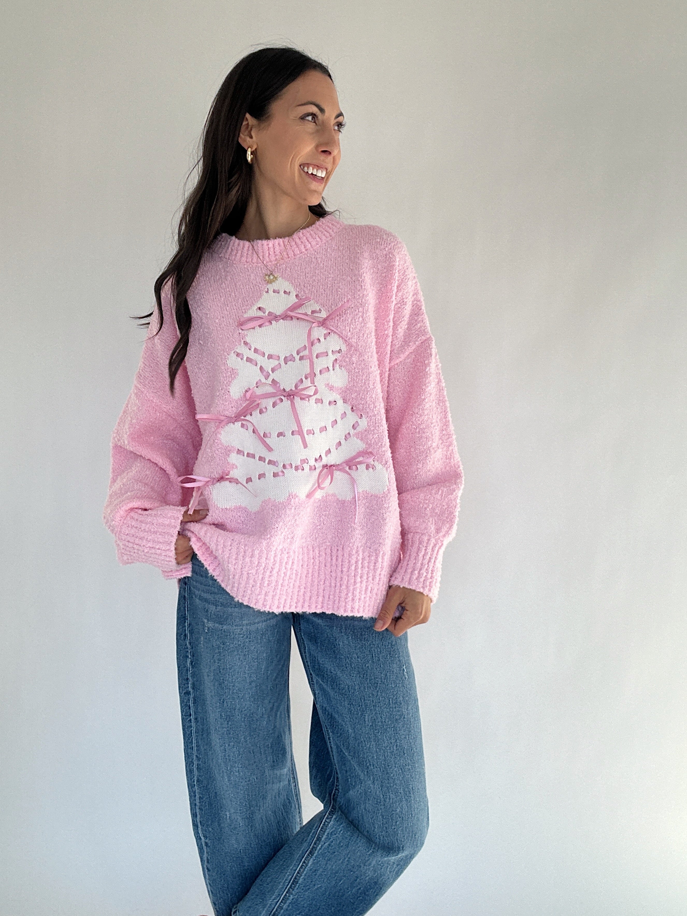 Woman wearing a pink sweater with a white tree design against a plain background