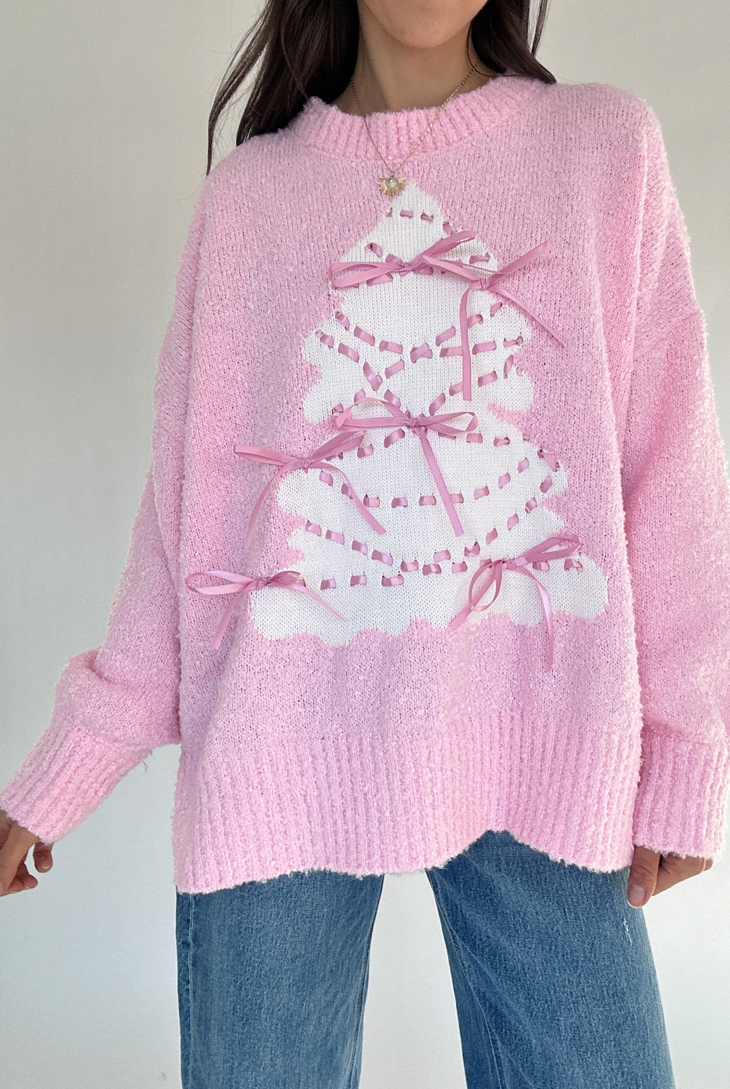 Person wearing a pink sweater with a white tree design on a plain background
