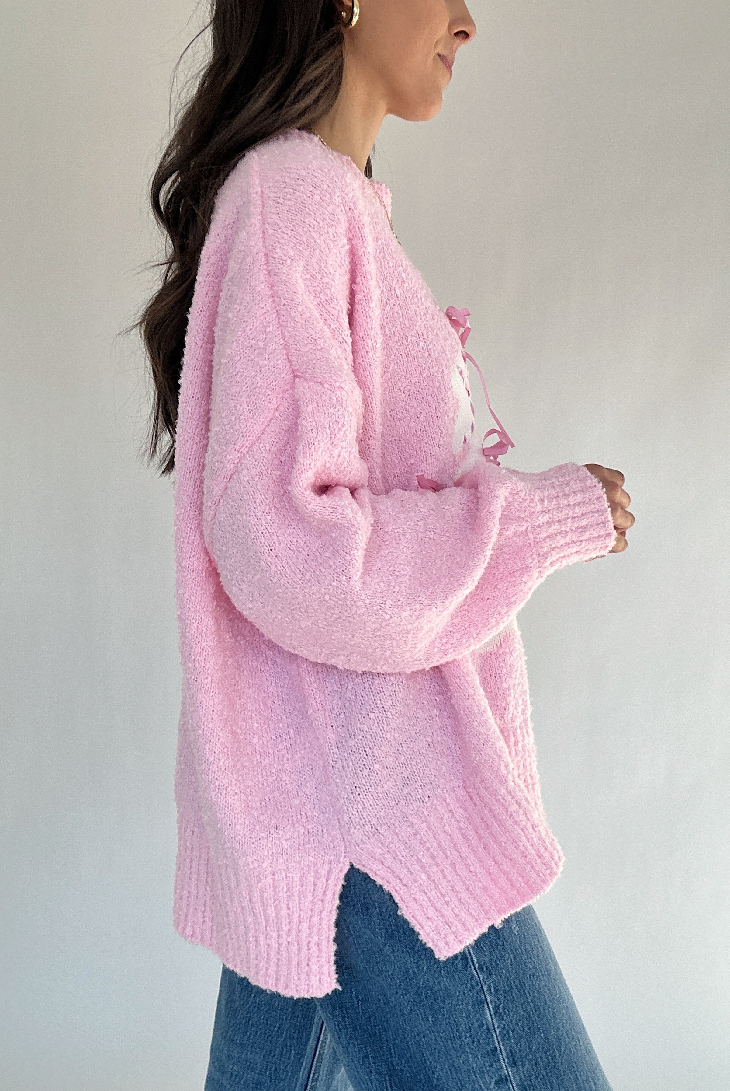 Person wearing a pink knitted sweater and blue jeans against a plain background from side