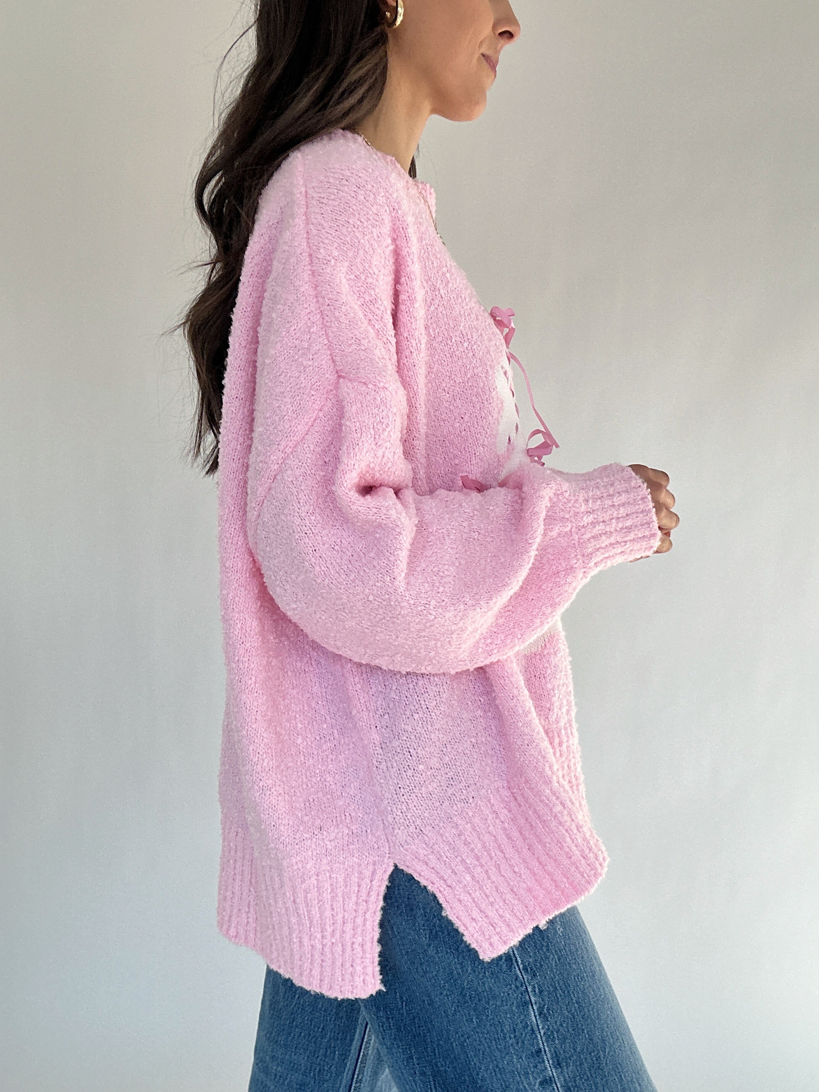 Person wearing a pink knitted sweater and blue jeans against a plain background from side