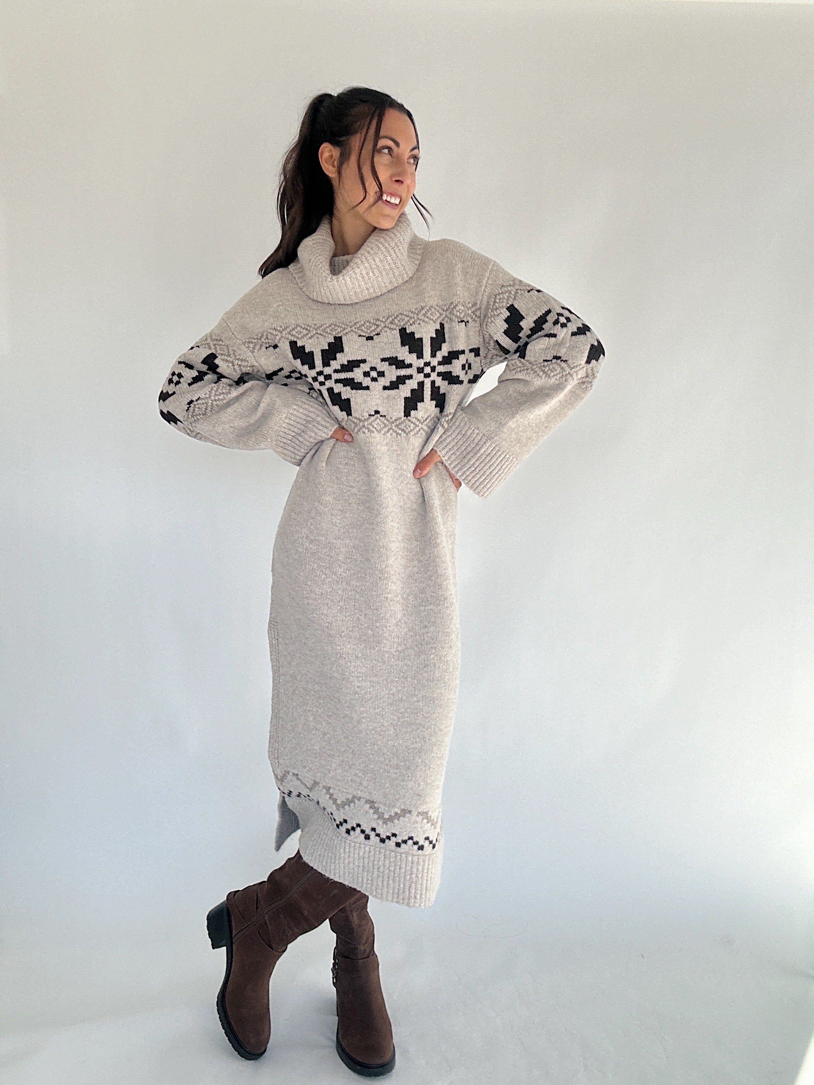 Woman wearing a long beige sweater with a pattern, standing against a white background
