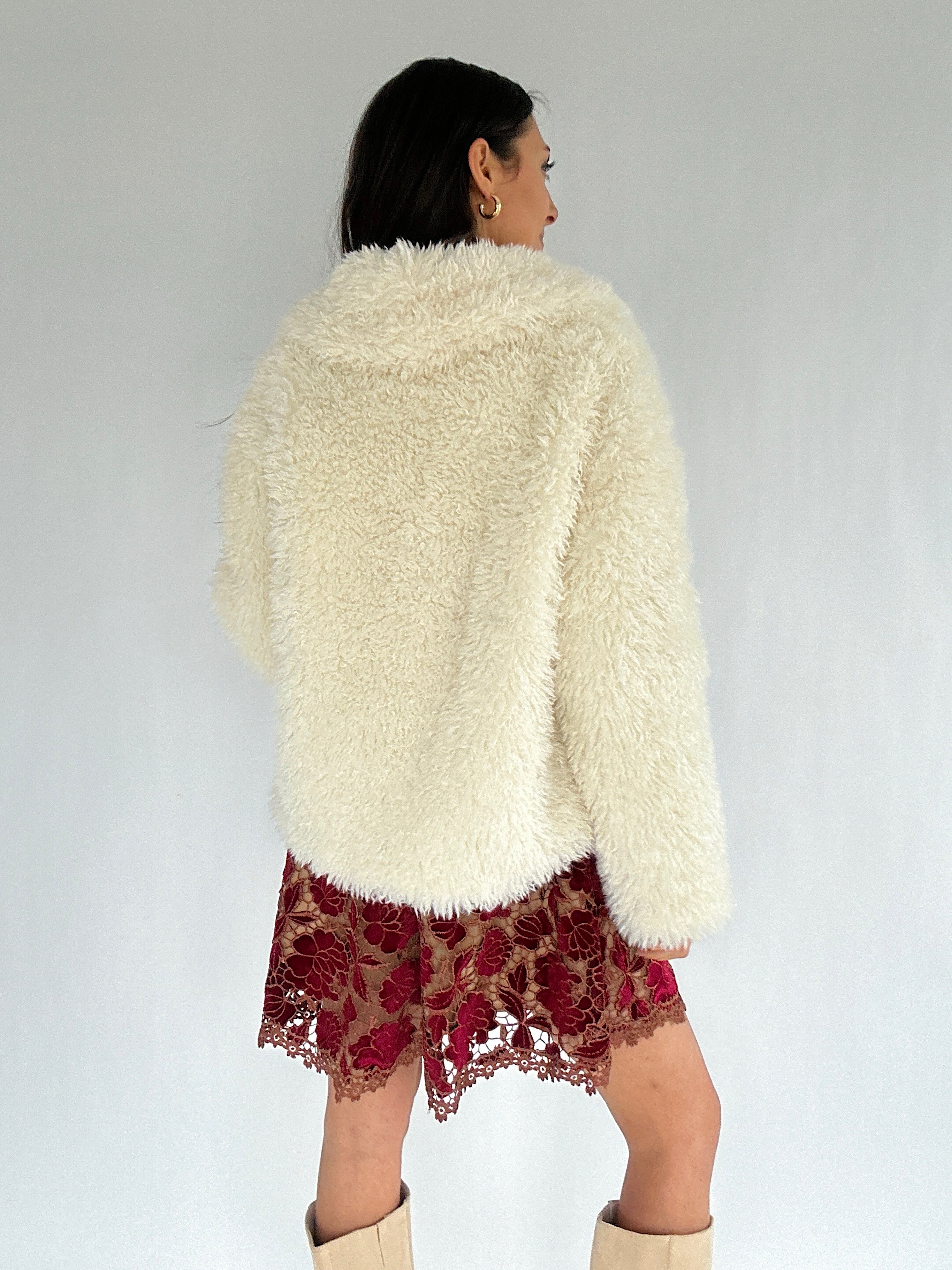 Person wearing a faux fur white jacket over a red lace dress on a plain background