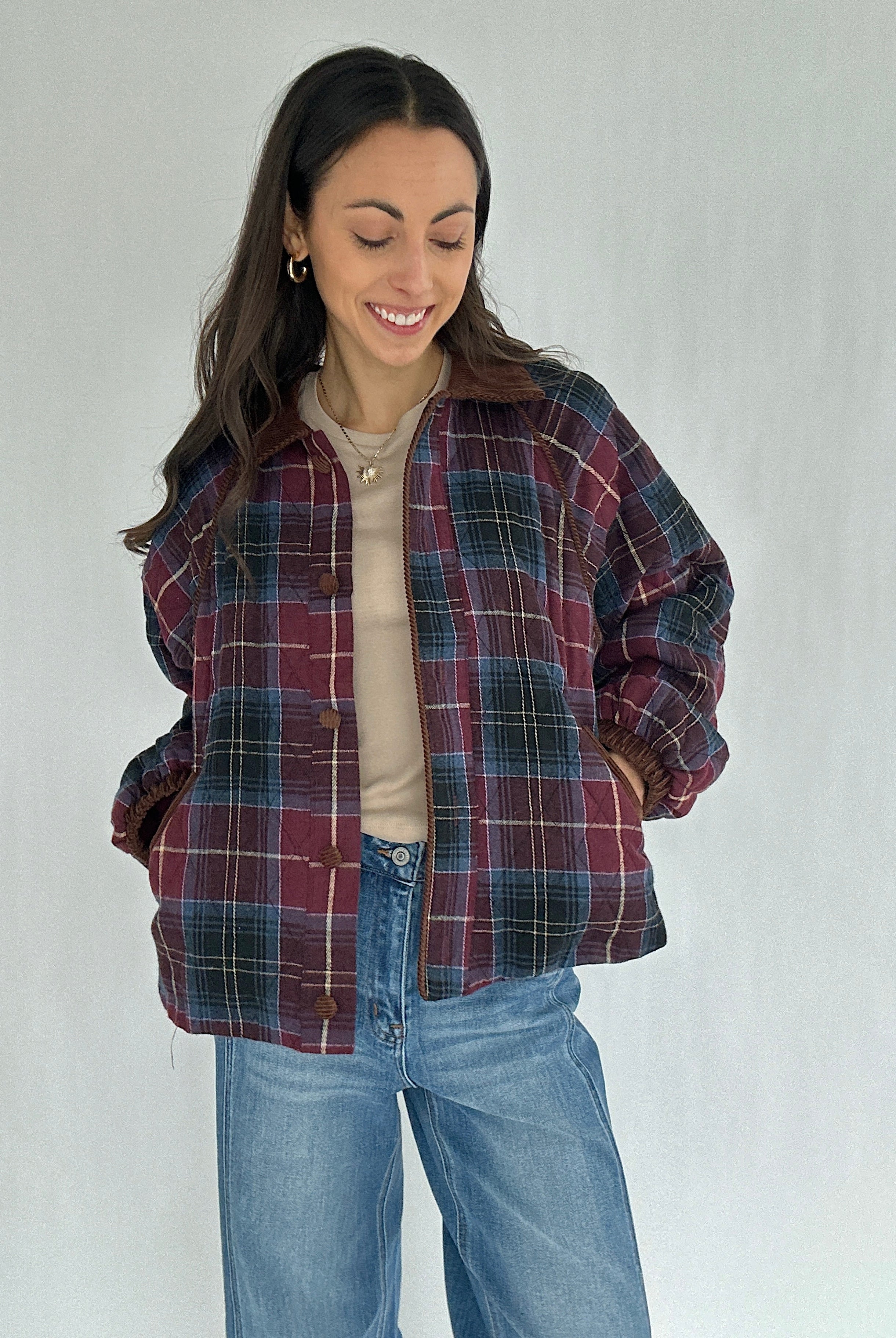 Woman wearing a maroon plaid jacket and jeans on a plain background