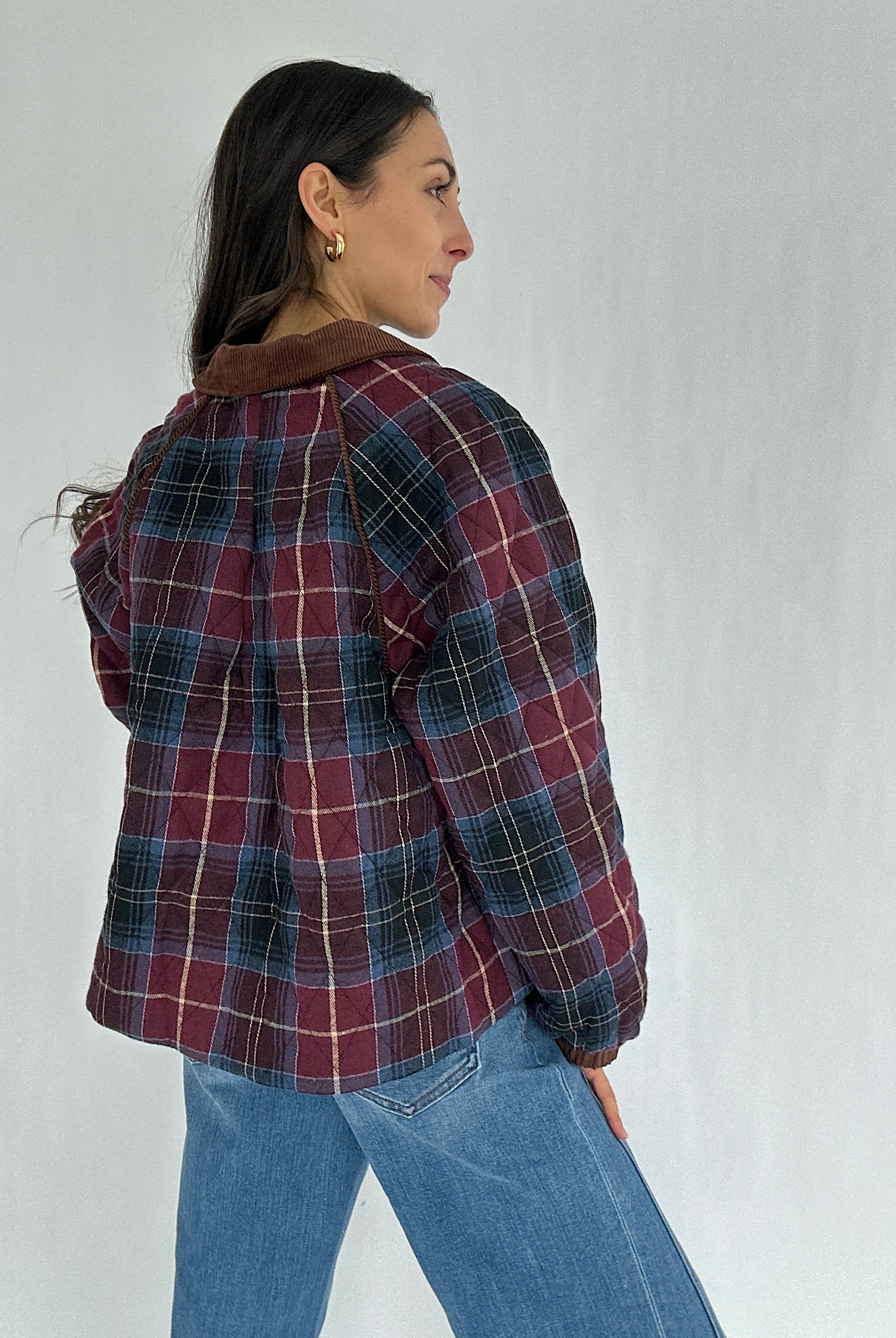 Person wearing a maroon plaid jacket and jeans against a plain background showing the back