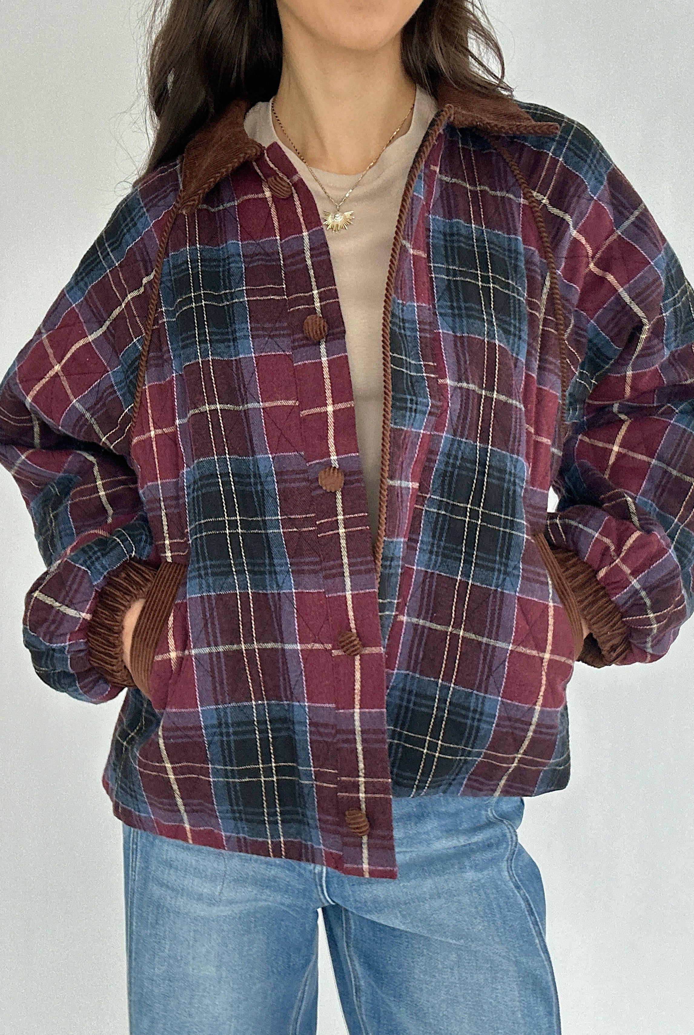 Person wearing a maroon plaid jacket with hands in pockets against a neutral background