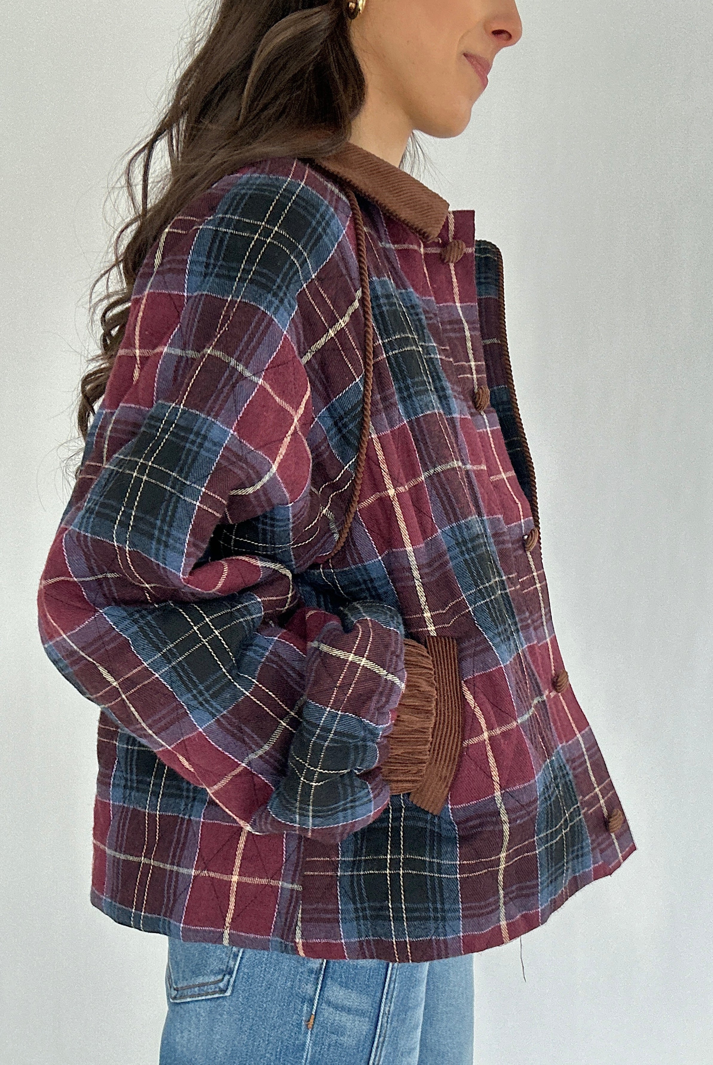 Person wearing a plaid jacket with corduroy accents on a plain background showing hands in side pockets