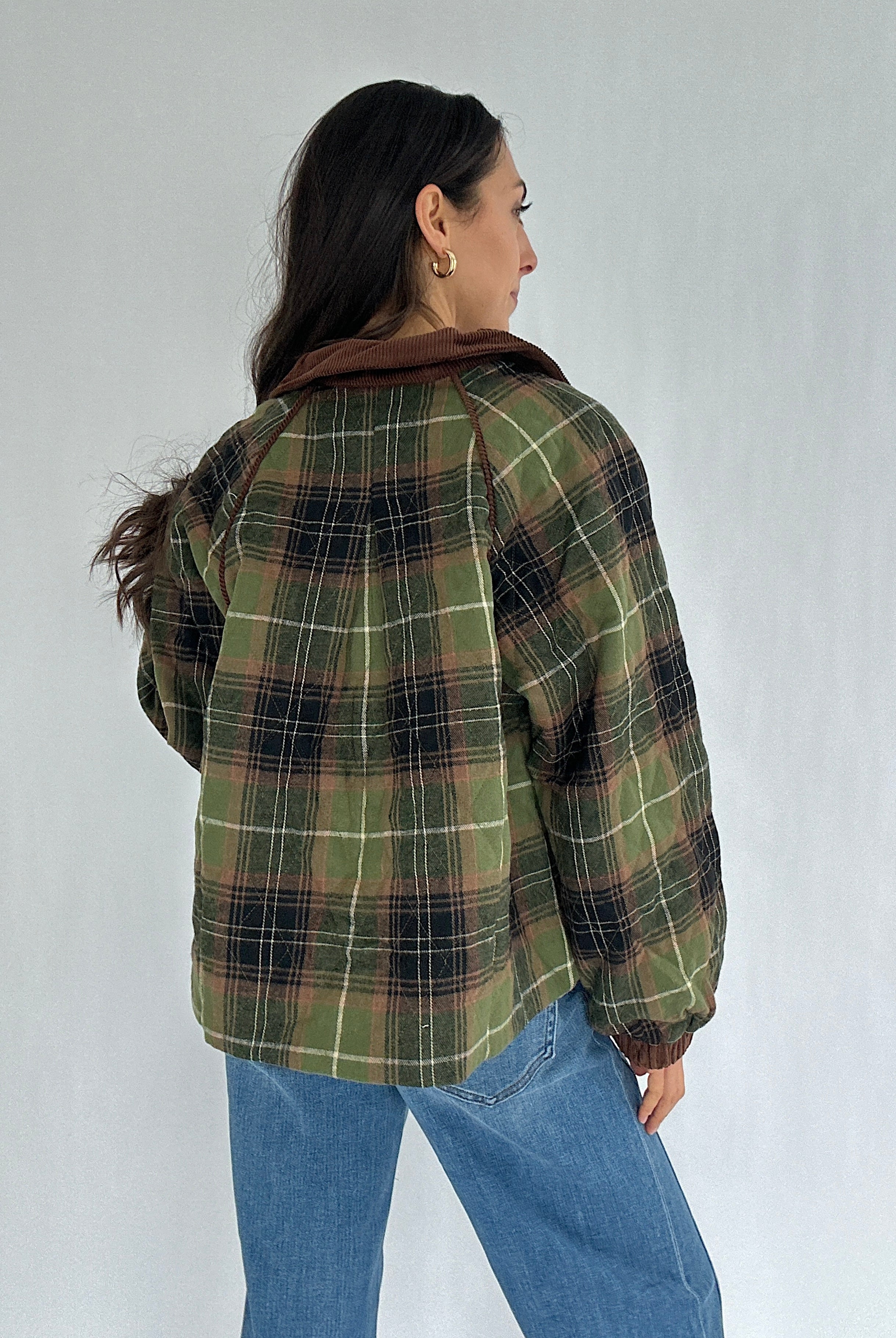 Person wearing a green plaid jacket and blue jeans against a white background showing back
