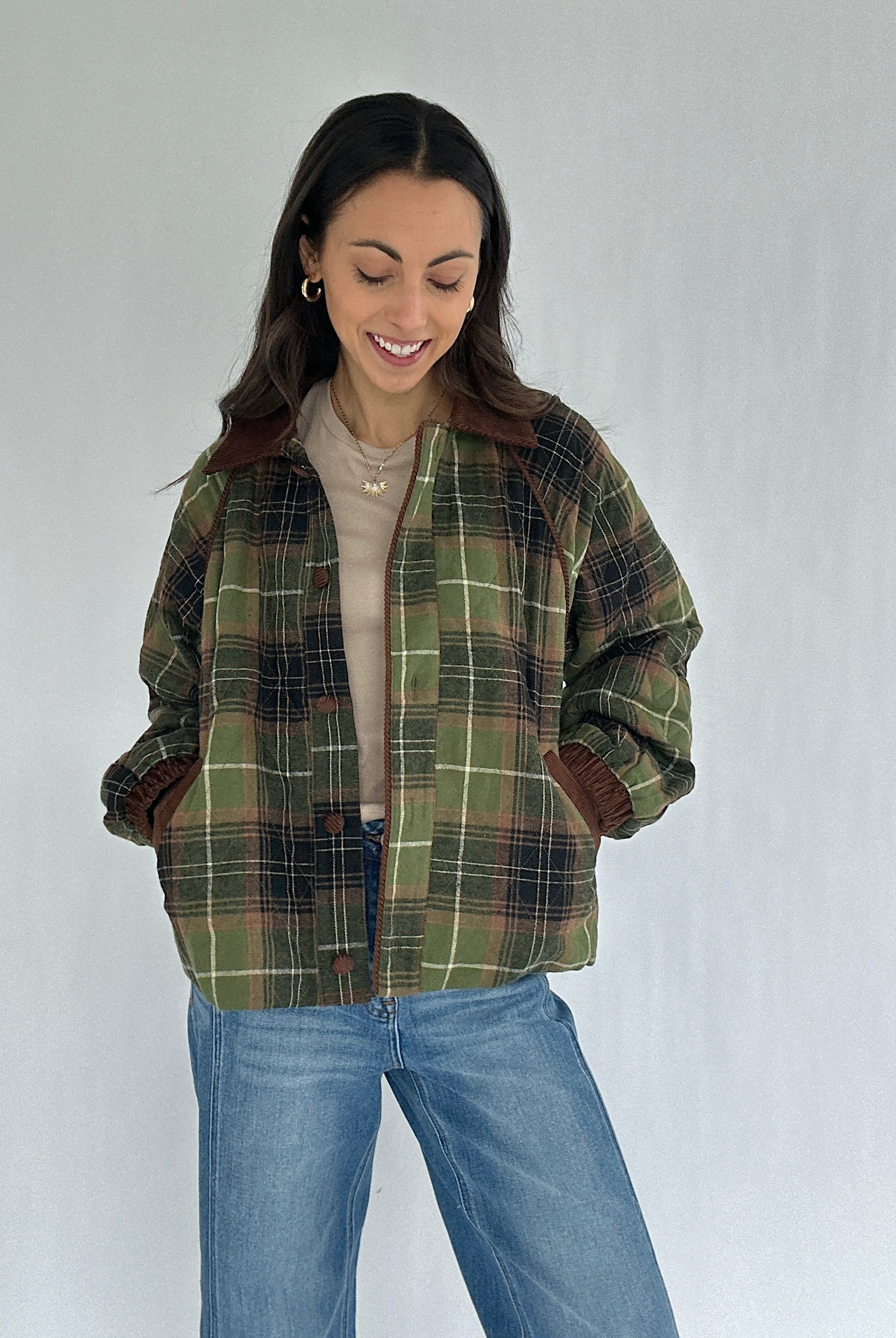 Woman wearing a green plaid jacket and jeans against a plain background with hands in pockets