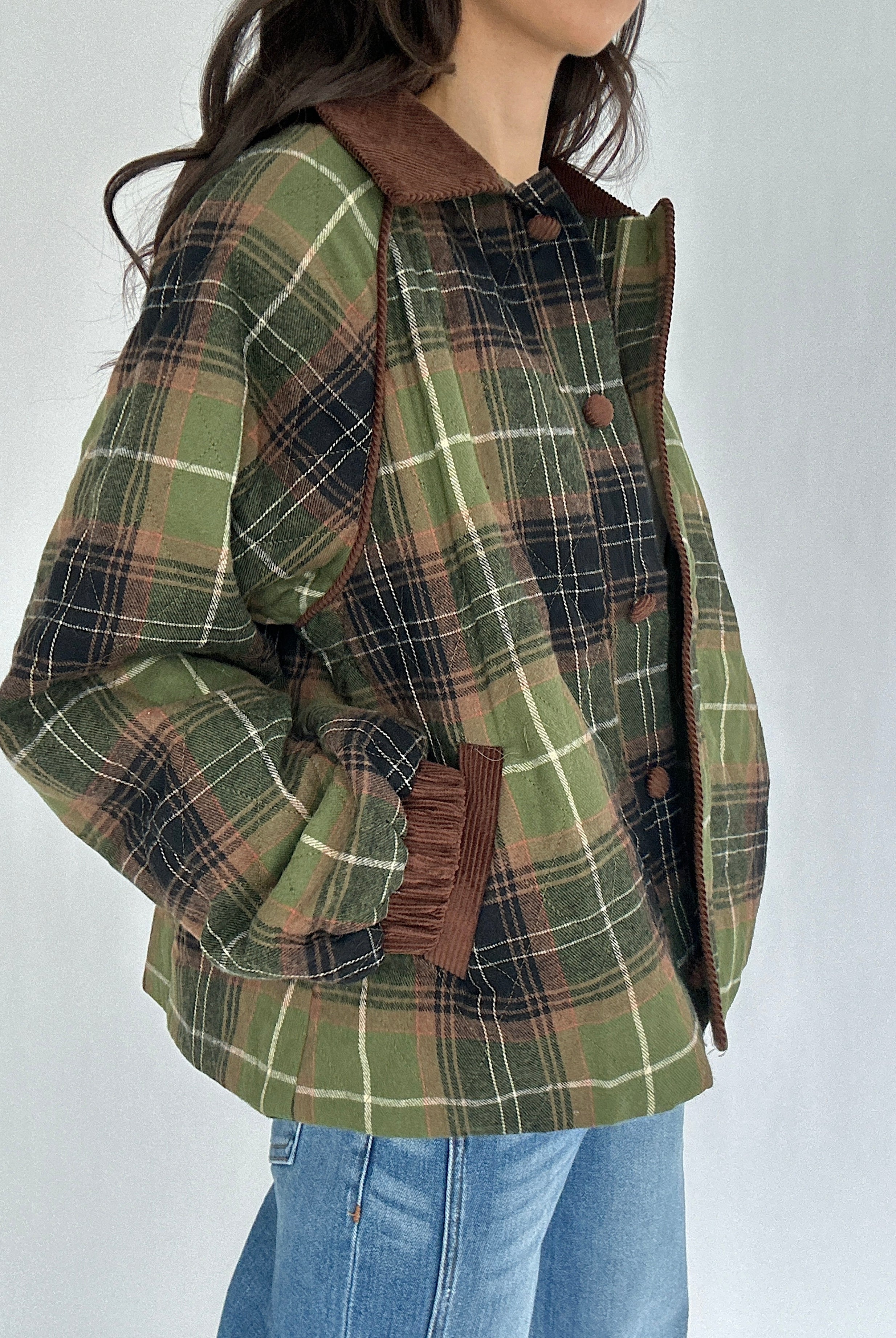 Green plaid jacket with brown accents worn by a person on a white background with hands in pockets