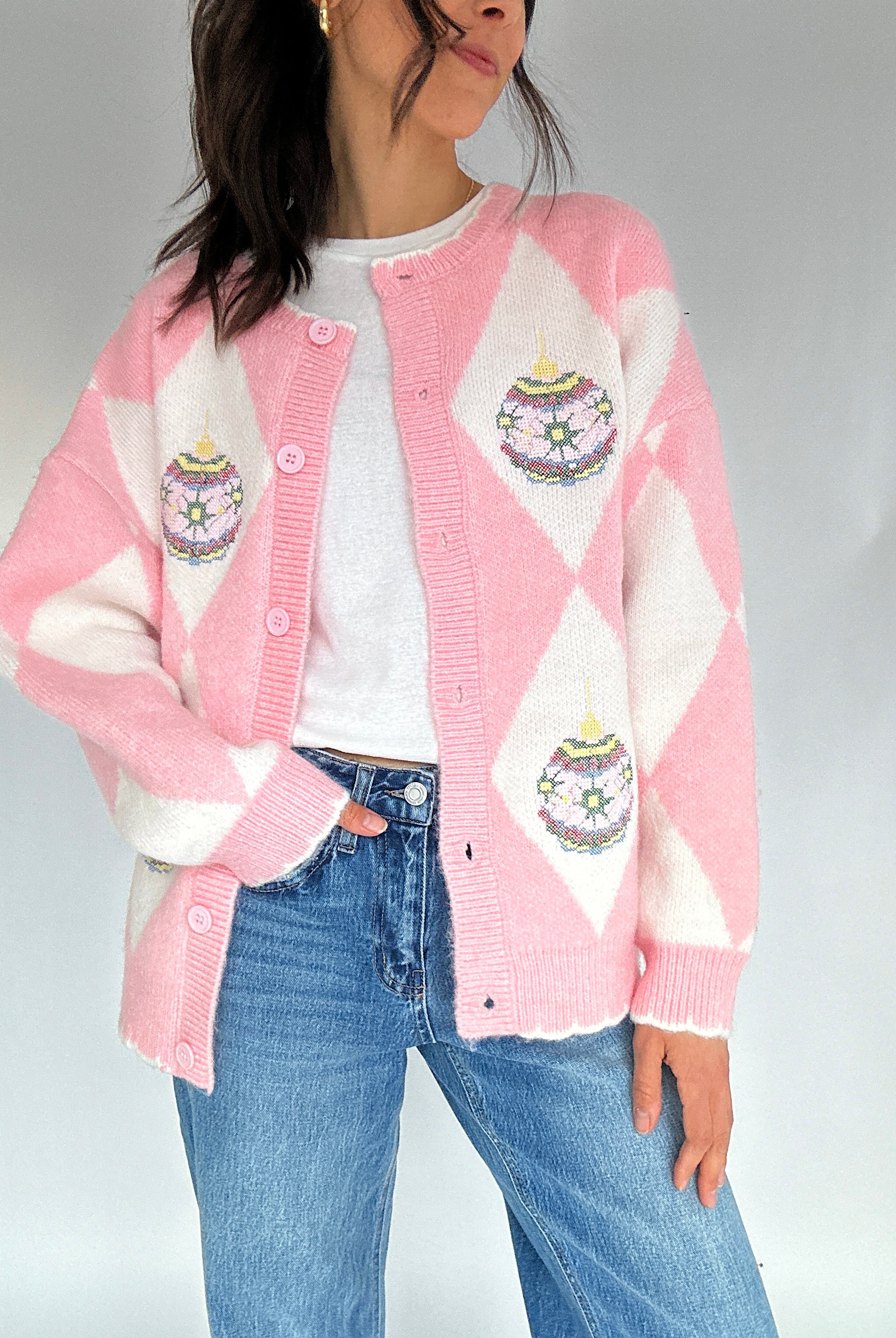 Person wearing a pink and white argyle cardigan with embroidered ornament designs on a plain background