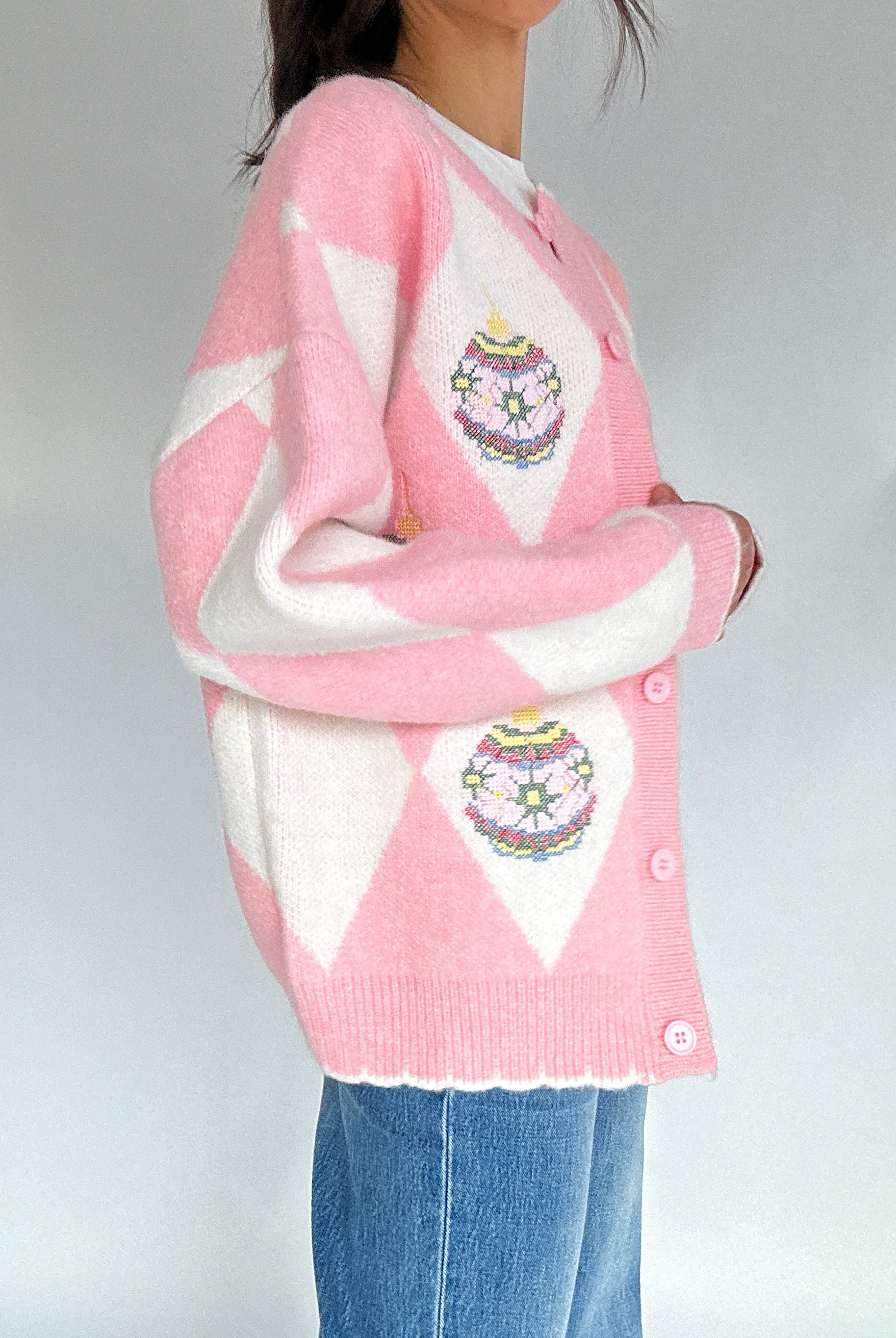 Person wearing a pink and white argyle cardigan with ornament designs on a plain background from side