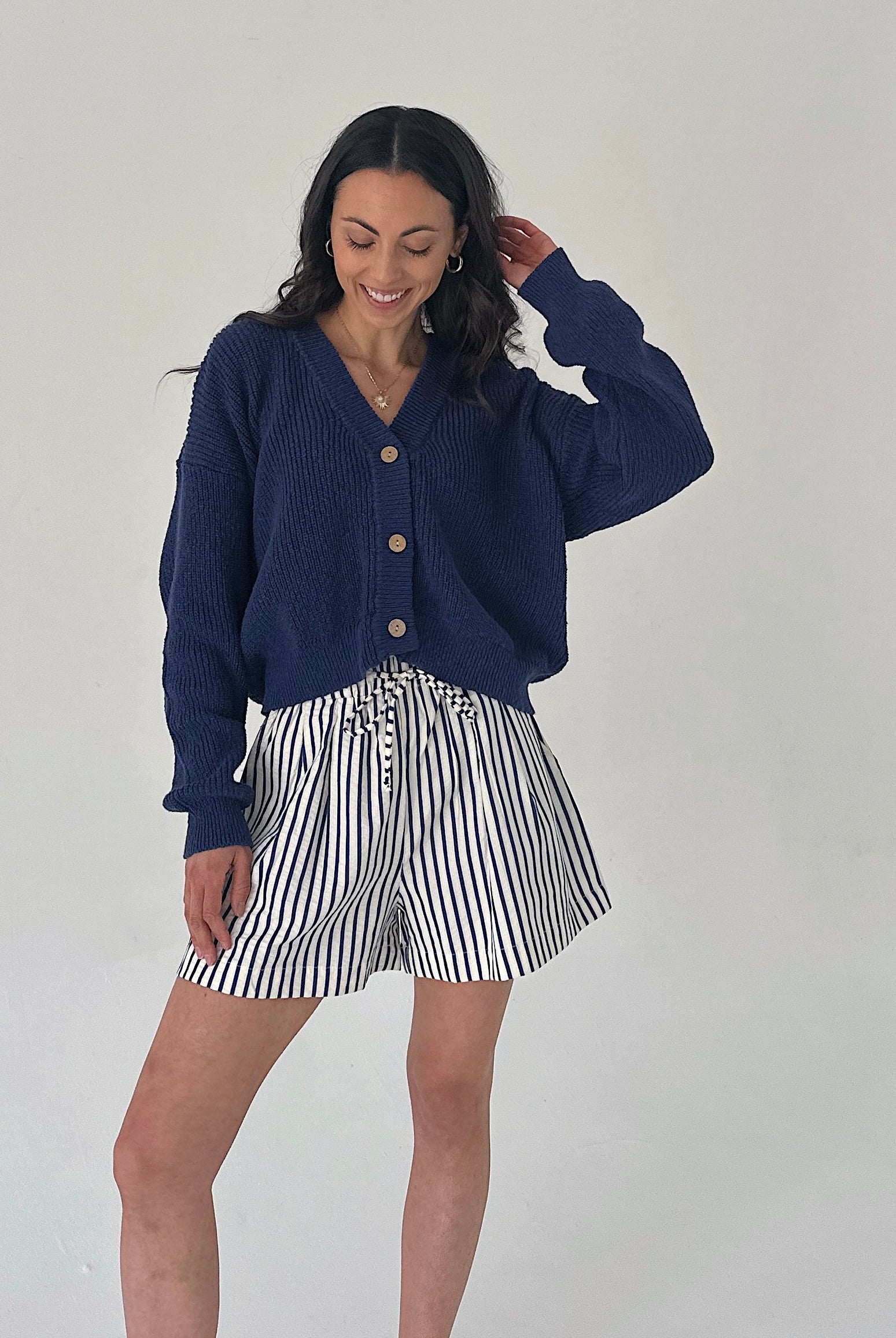 Woman wearing a navy cardigan and striped shorts against a white background