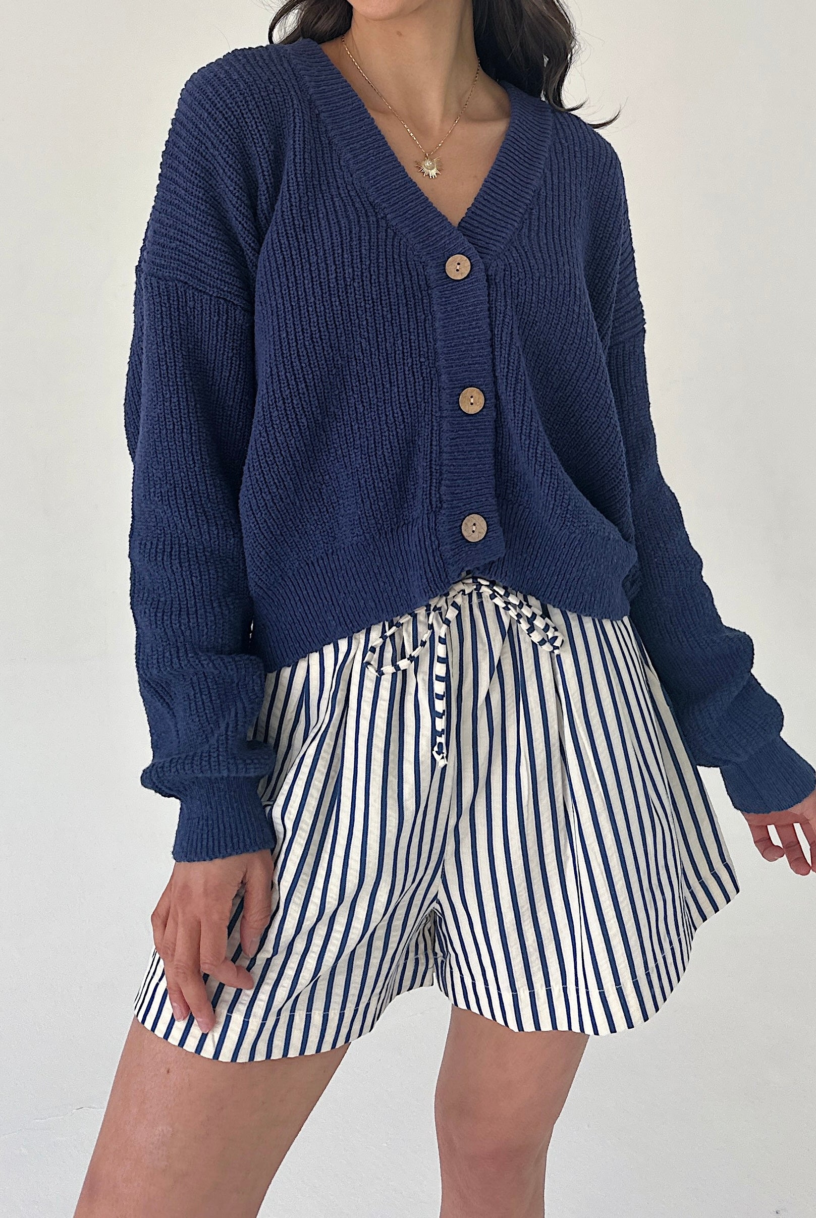 Person wearing a blue cardigan and striped shorts on a white background