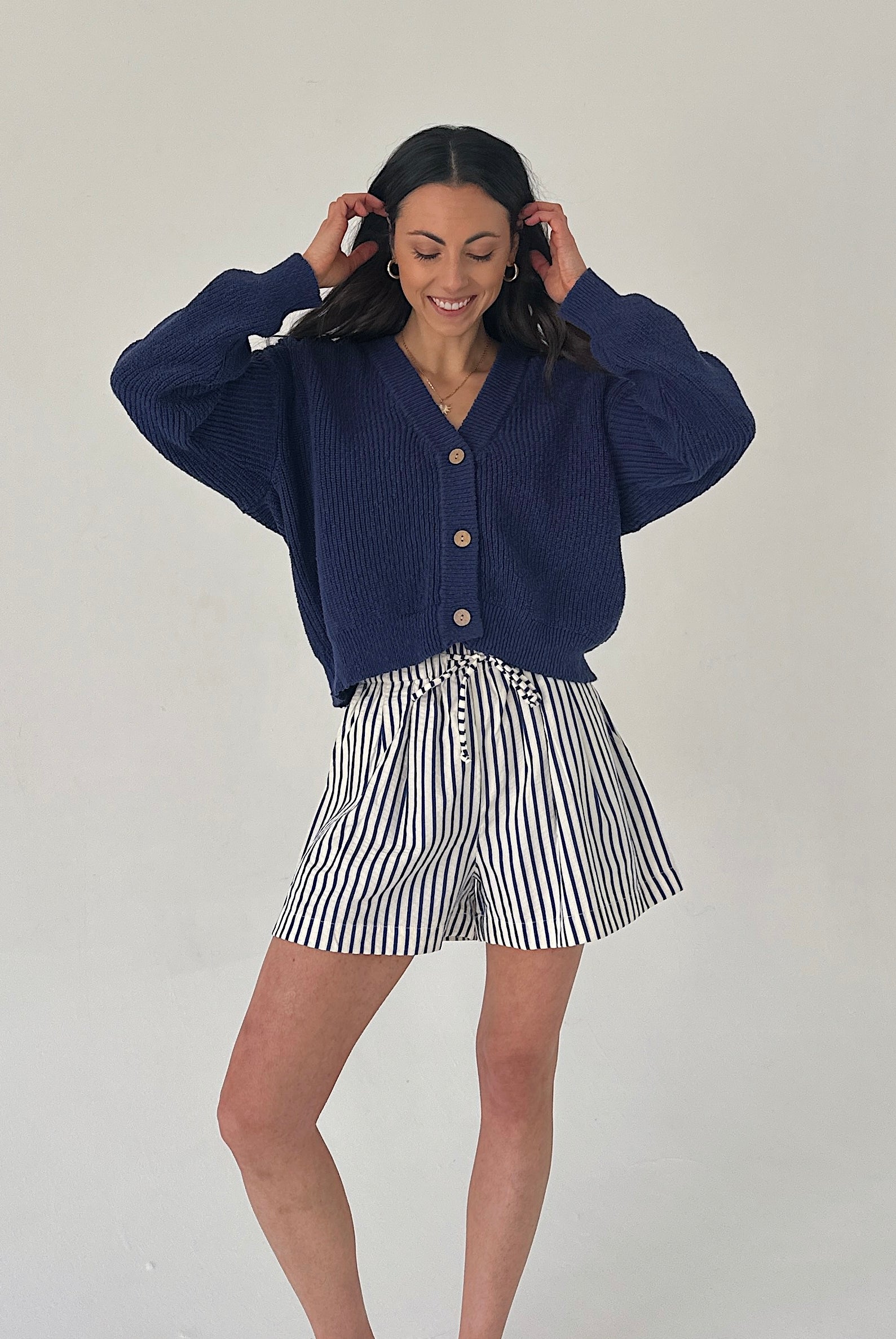 Woman wearing a navy blue cardigan and striped shorts on a plain background