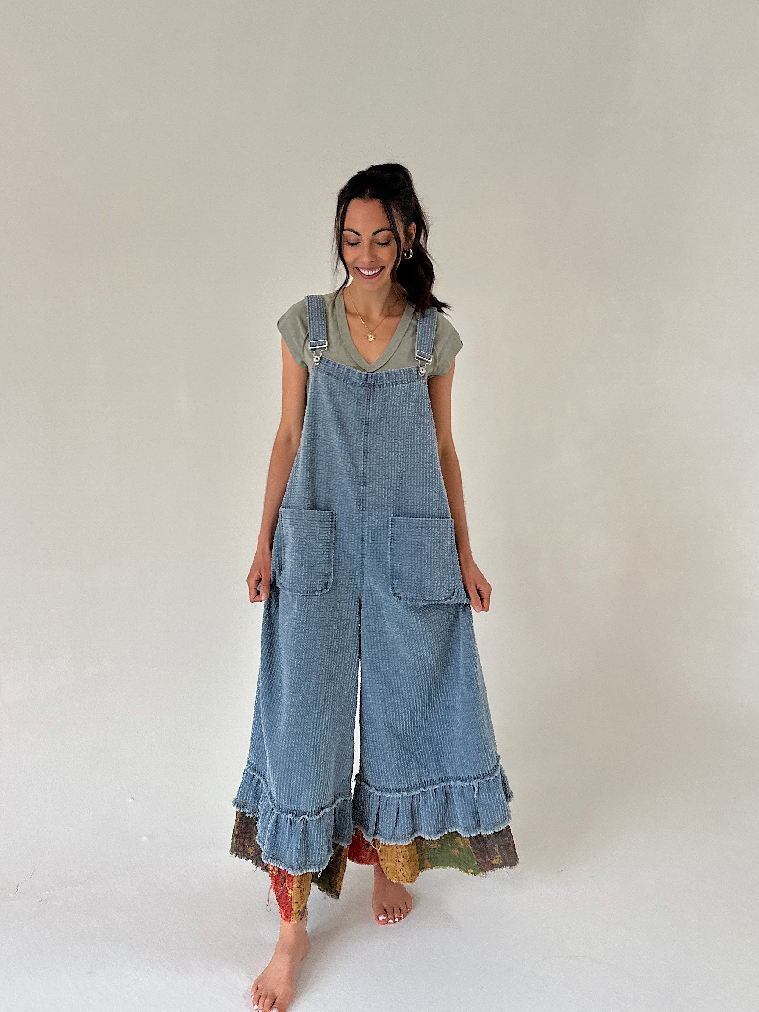 Woman wearing a denim overalls with ruffled hem on a plain background