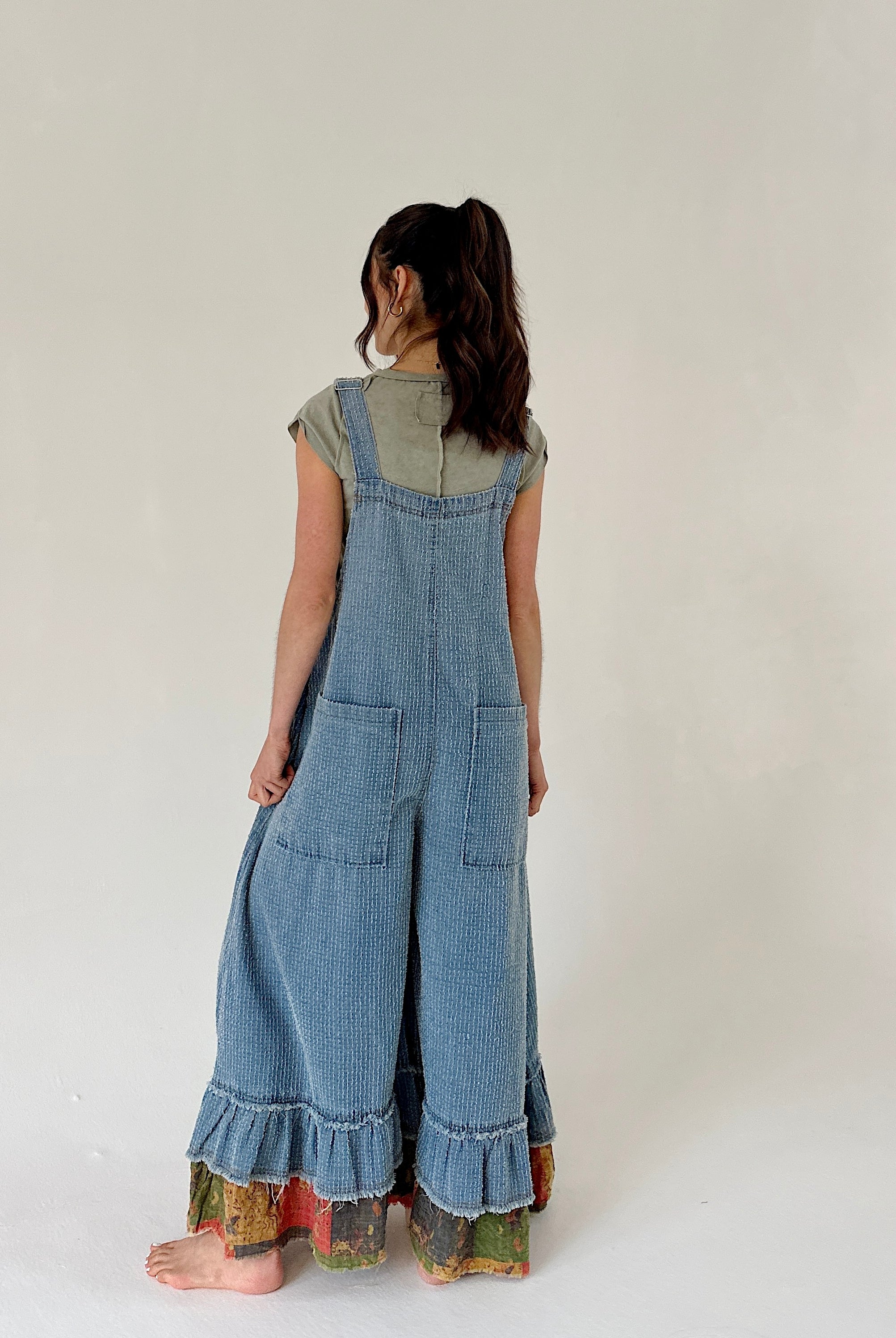 Person wearing a denim overalls from the back with a plain background