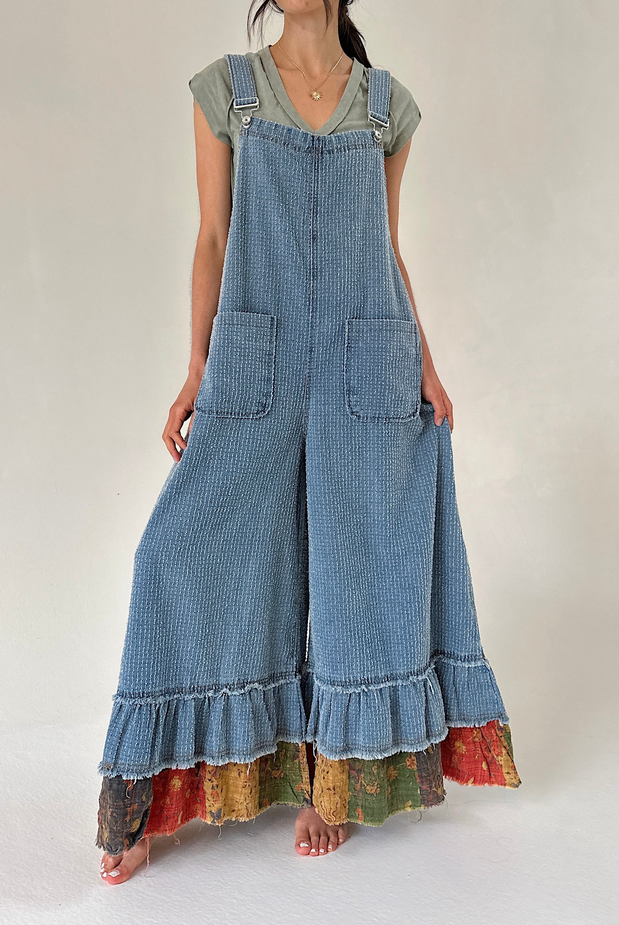 Person wearing a long denim overalls with ruffled bottom on a plain background
