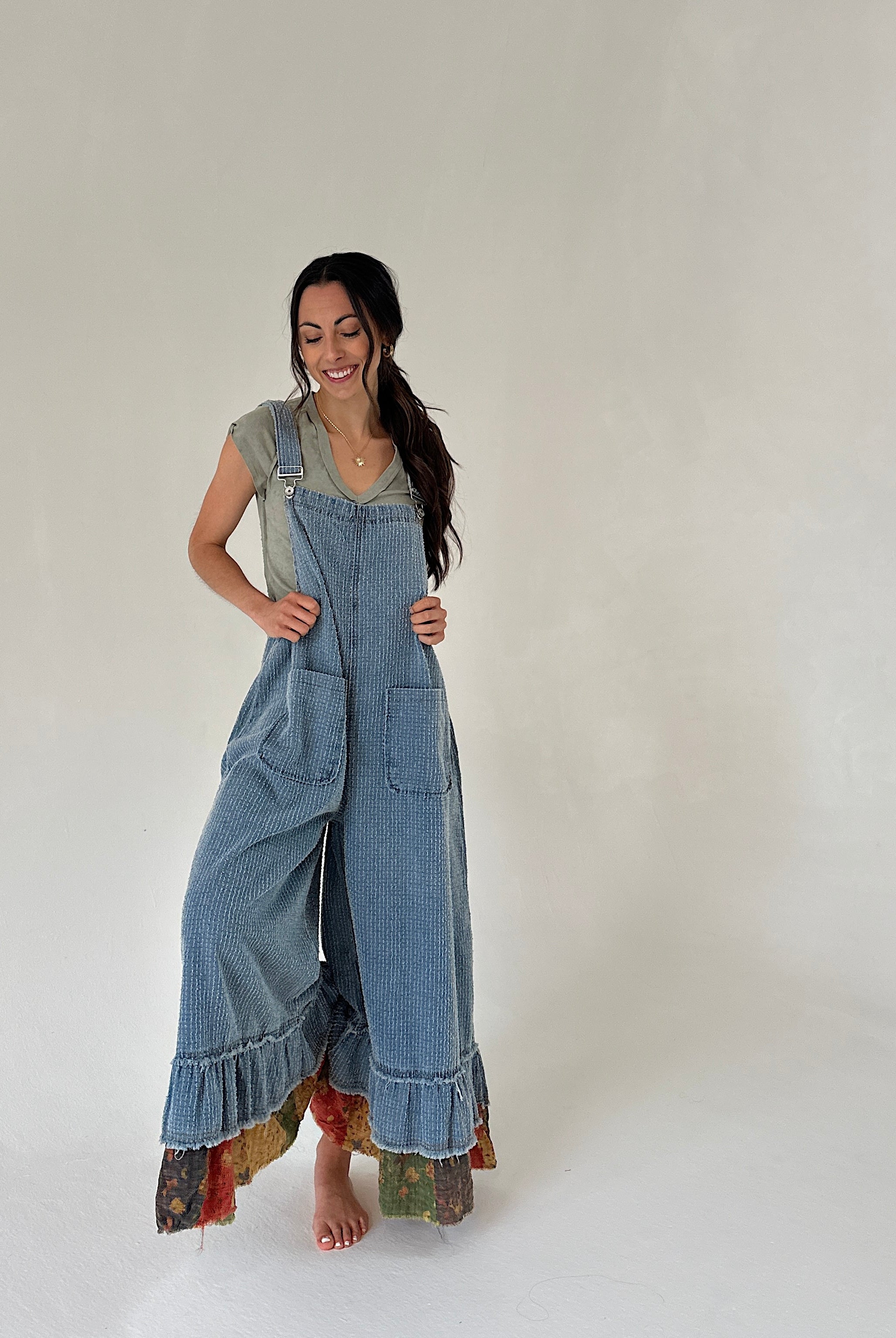 Woman wearing denim overalls with ruffled hem on a plain background