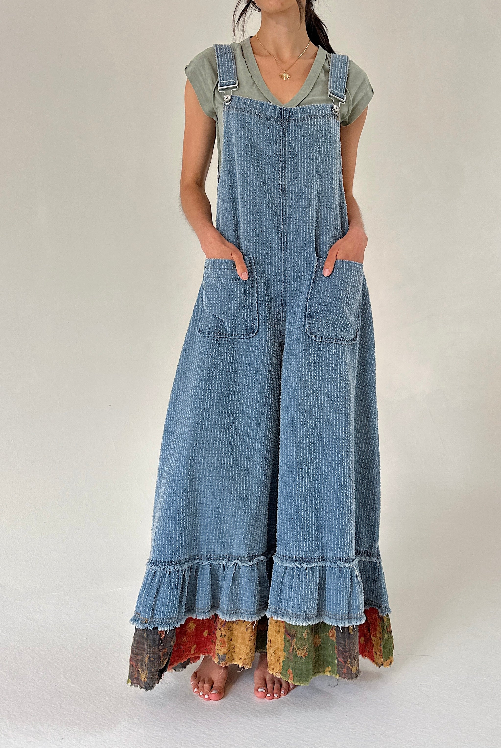 Person wearing denim overalls with colorful hem and front patch pockets on a white background