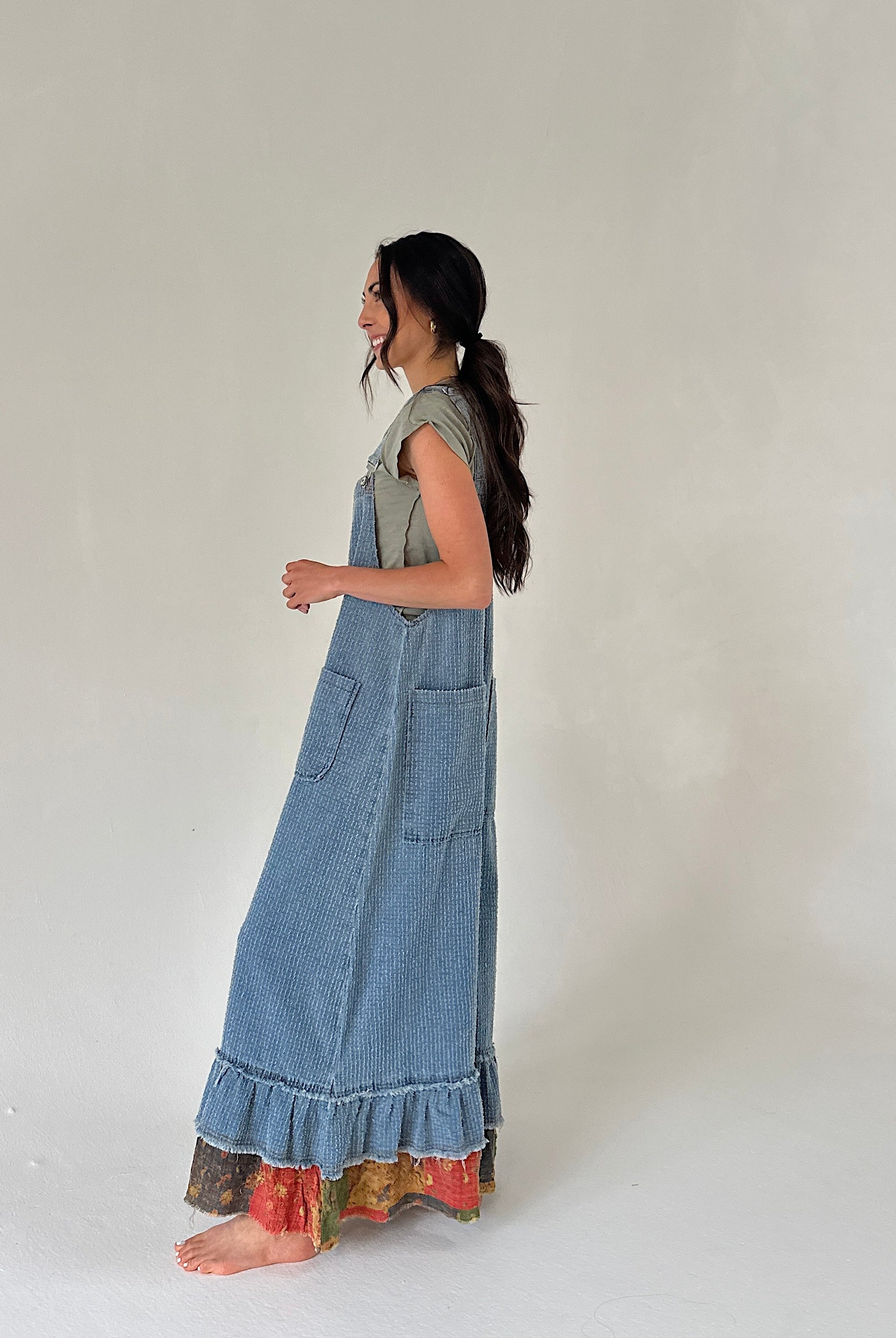 Woman denim overalls with a wide leg fit and ruffle hem from side with a plain background